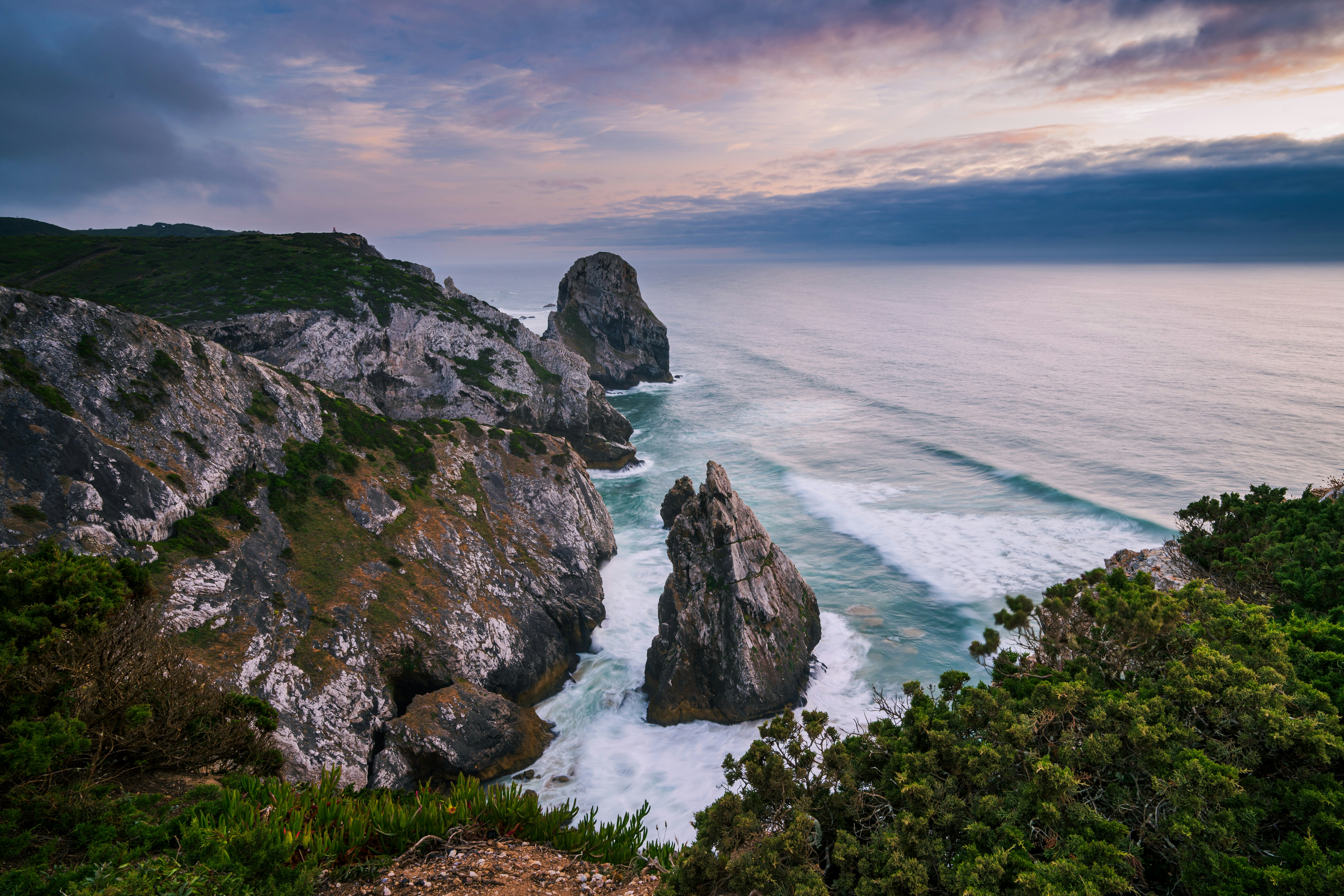 Coastal rocks face the ocean under a cloudy sky.