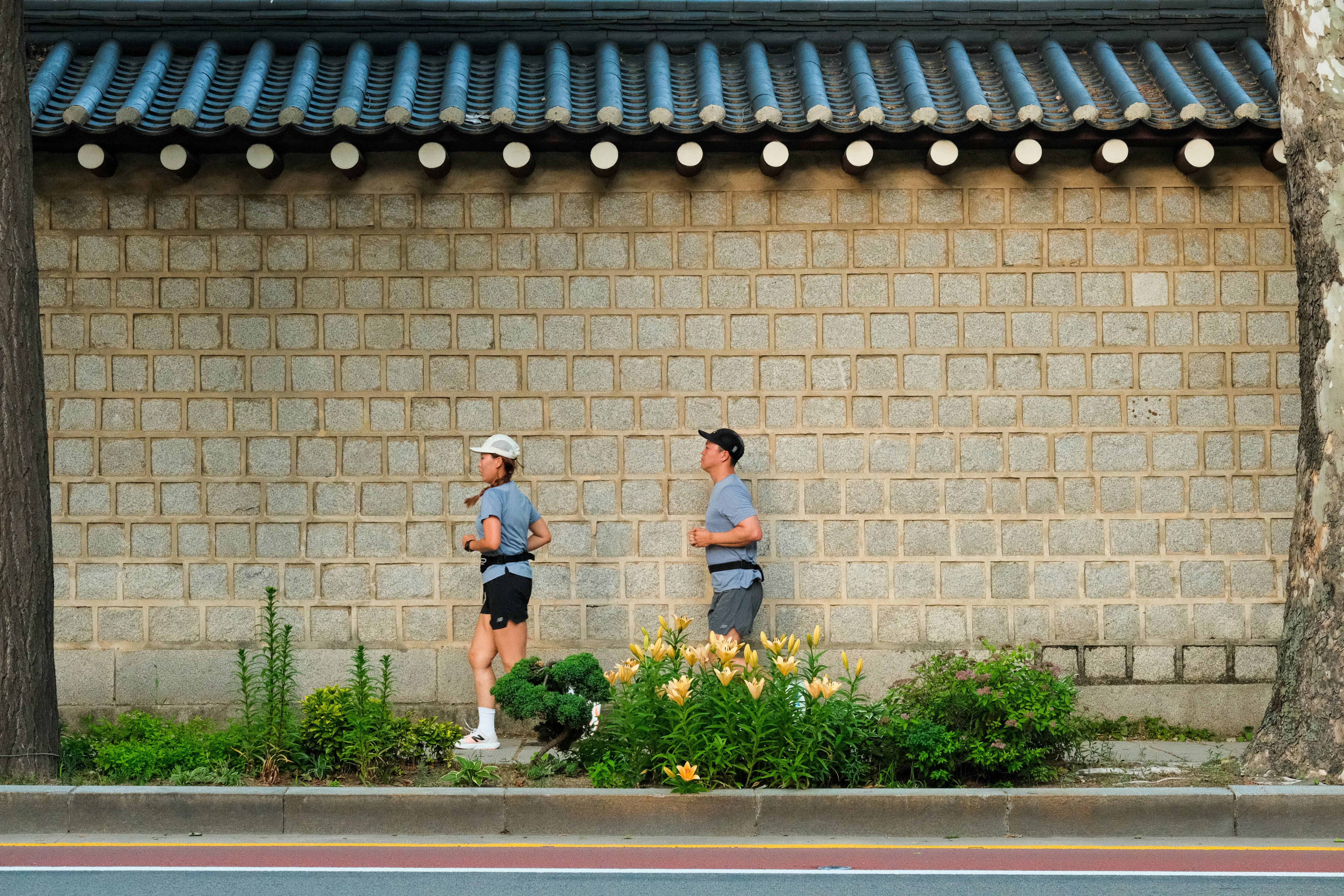 Two people are jogging in front of a wall.