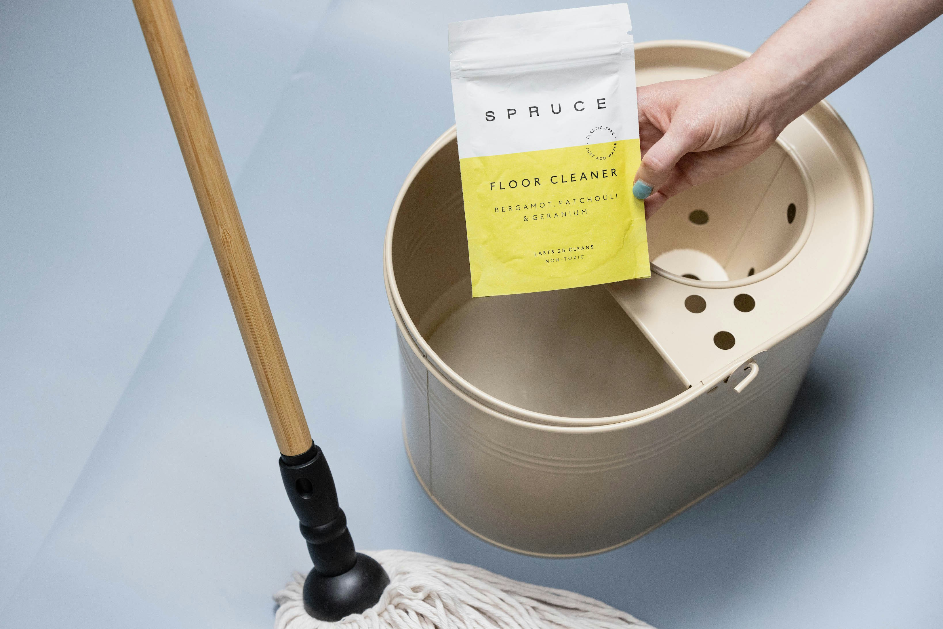 A person holds floor cleaner near a mop bucket.