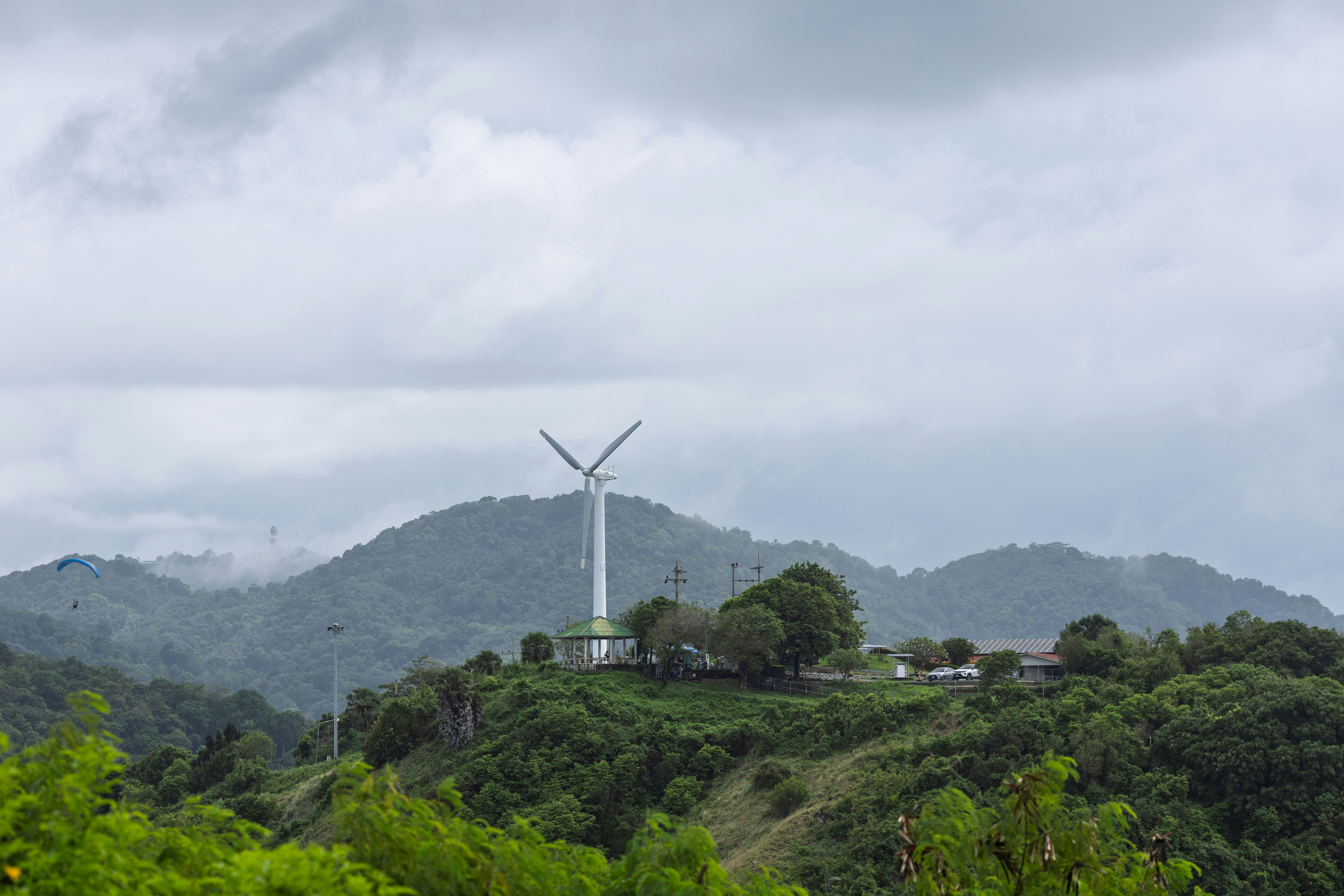 Wind turbine on a green hill with cloudy skies.