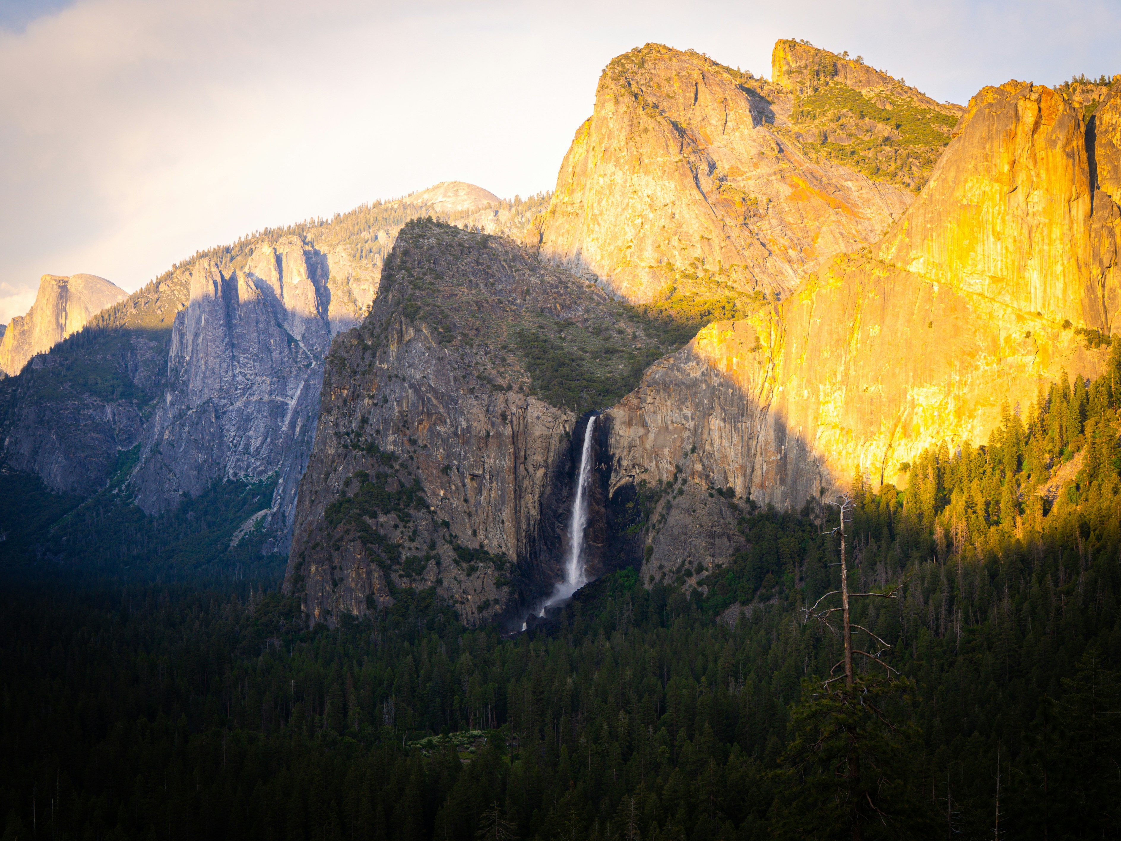 Waterfall cascades between towering mountains under sunlight.