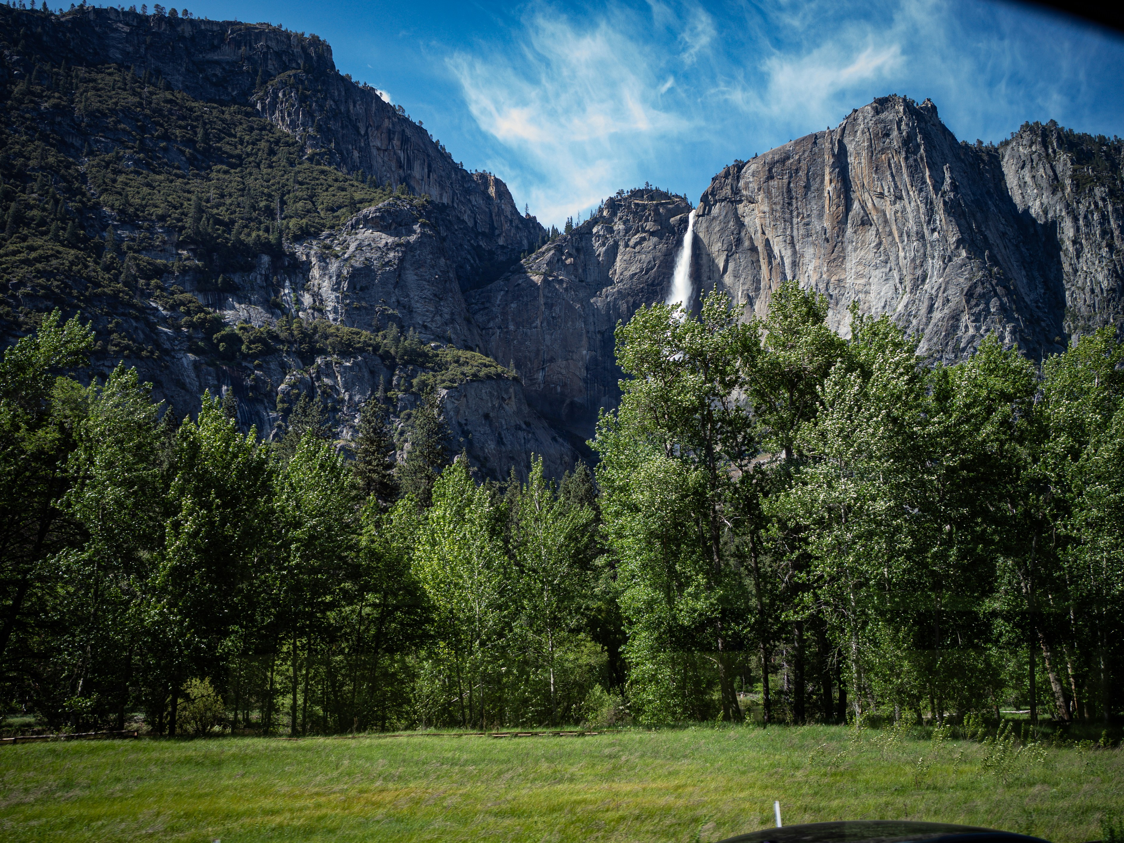 Mountains tower over a waterfall and trees.