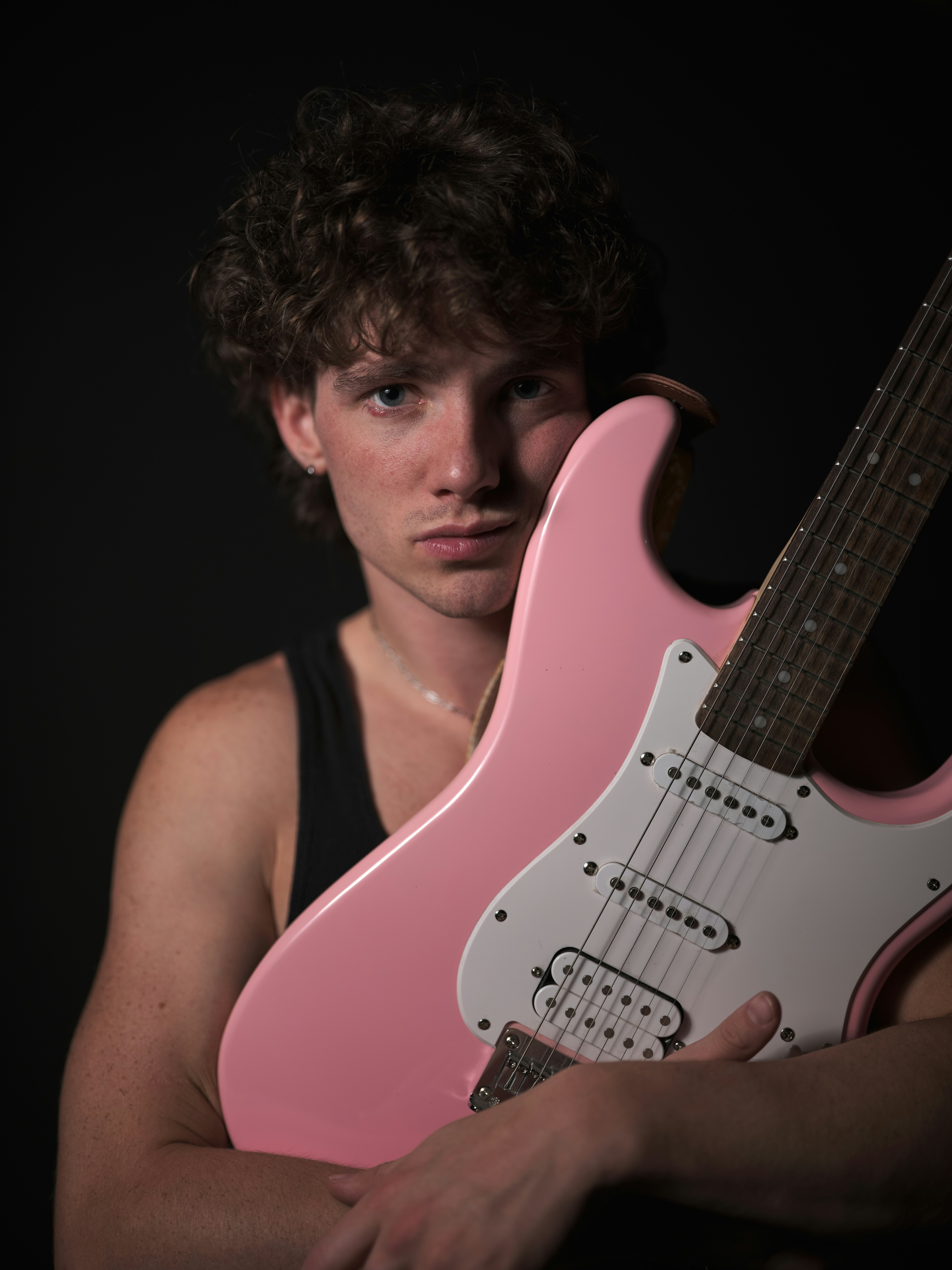 A young man poses with a pink guitar.