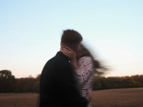 A blurry couple embraces and kisses outdoors.