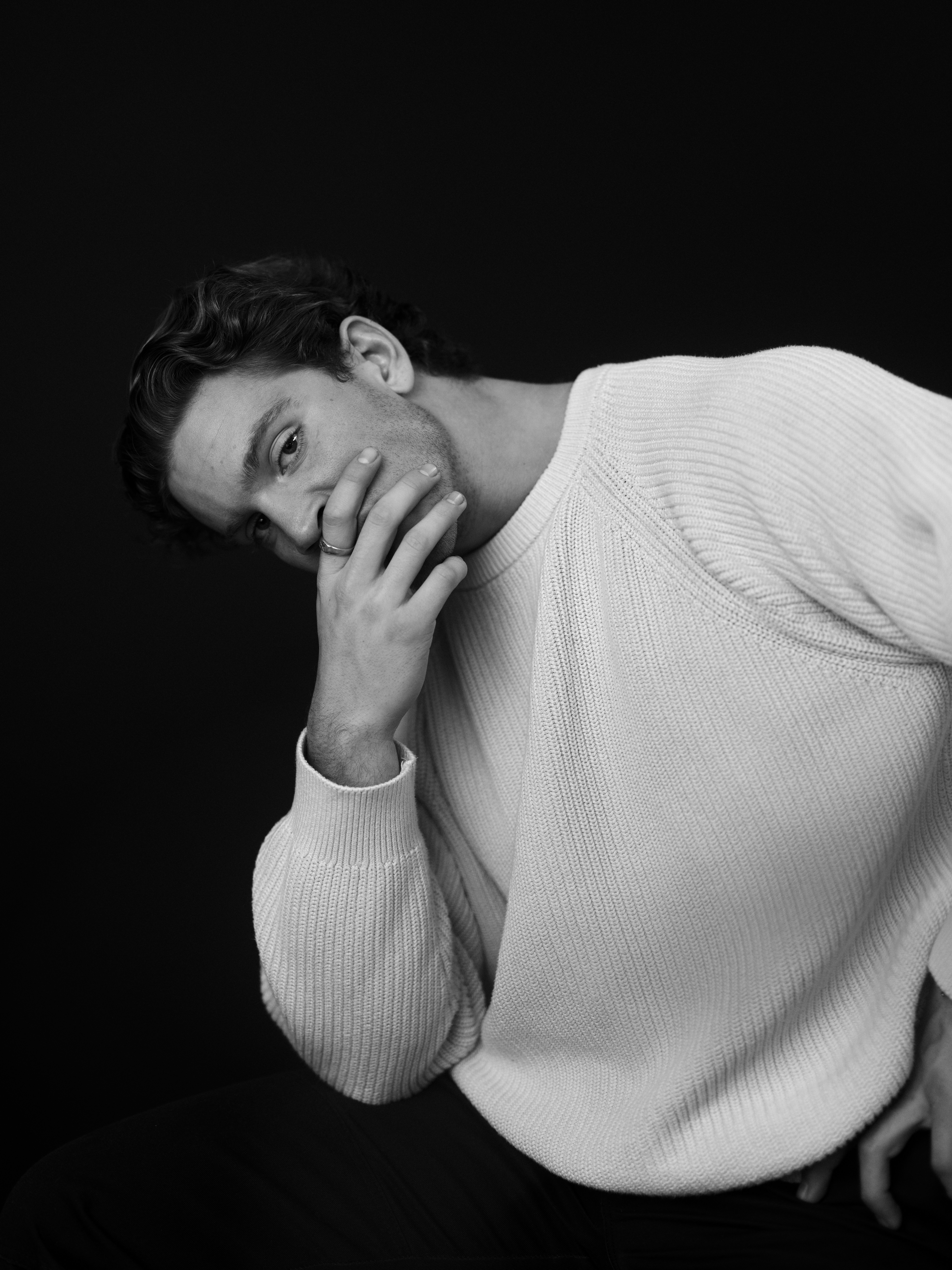 A man poses in a white sweater.