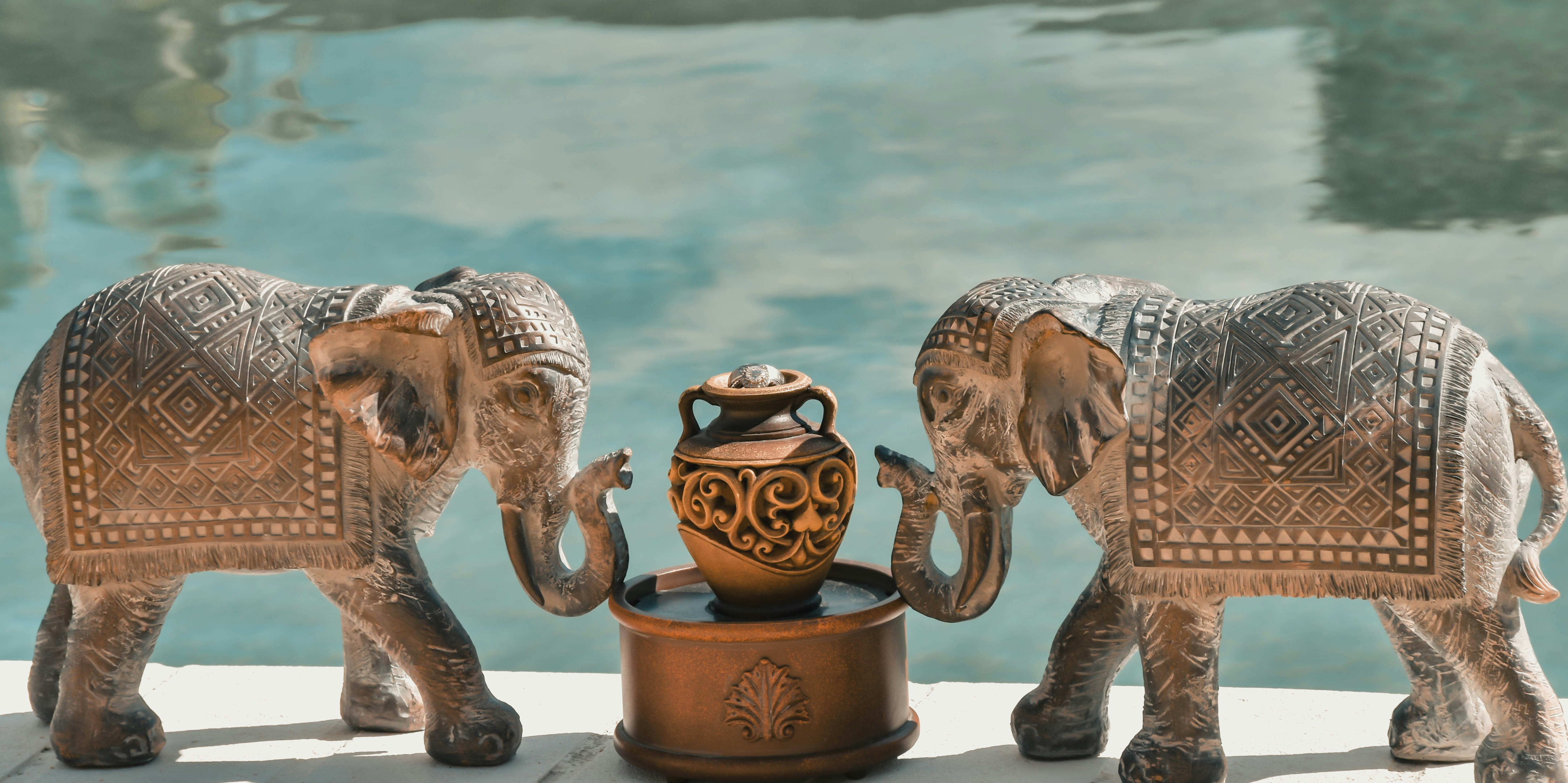 Two elephants flank a vase near a pool.