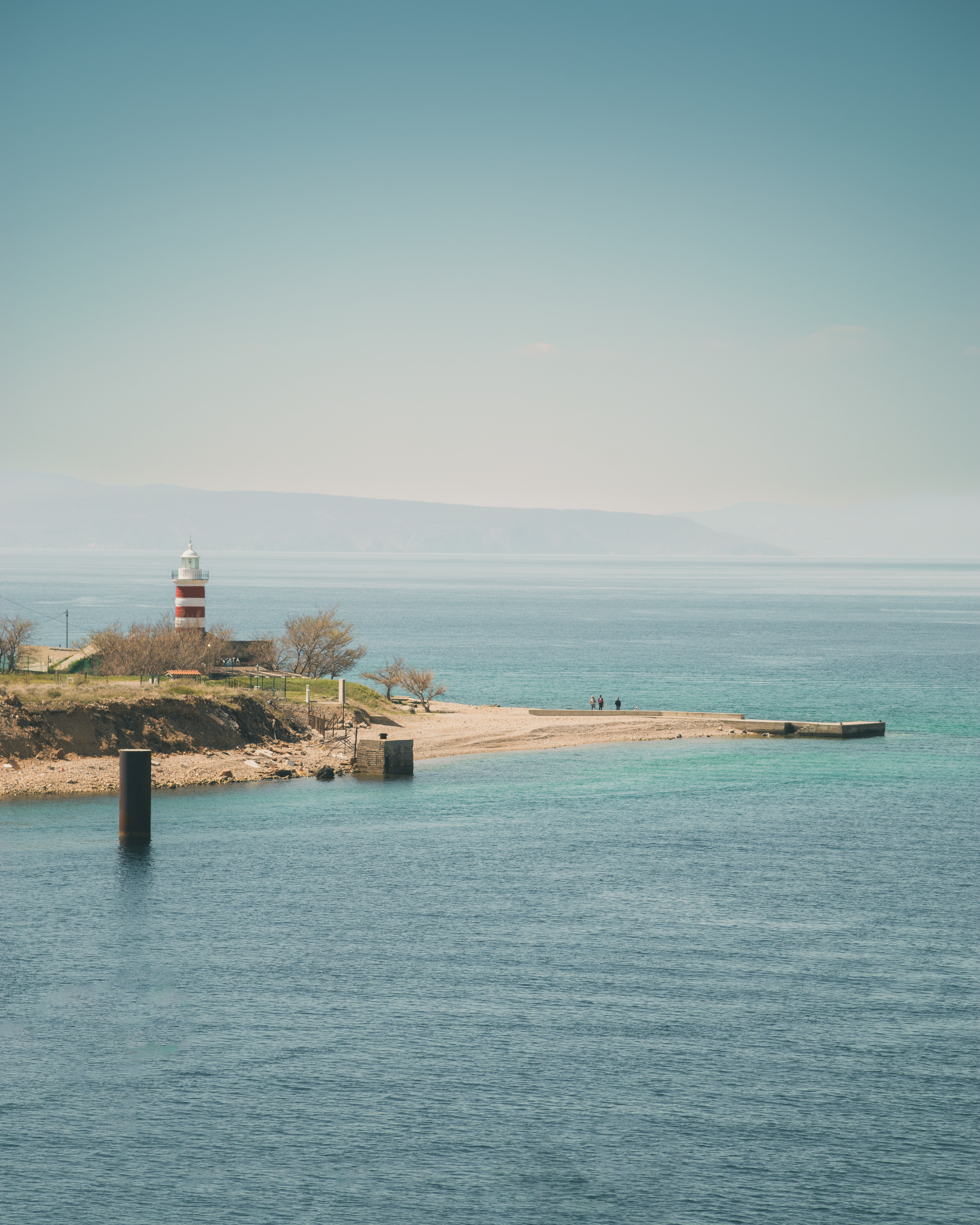 A lighthouse stands beside the calm ocean.