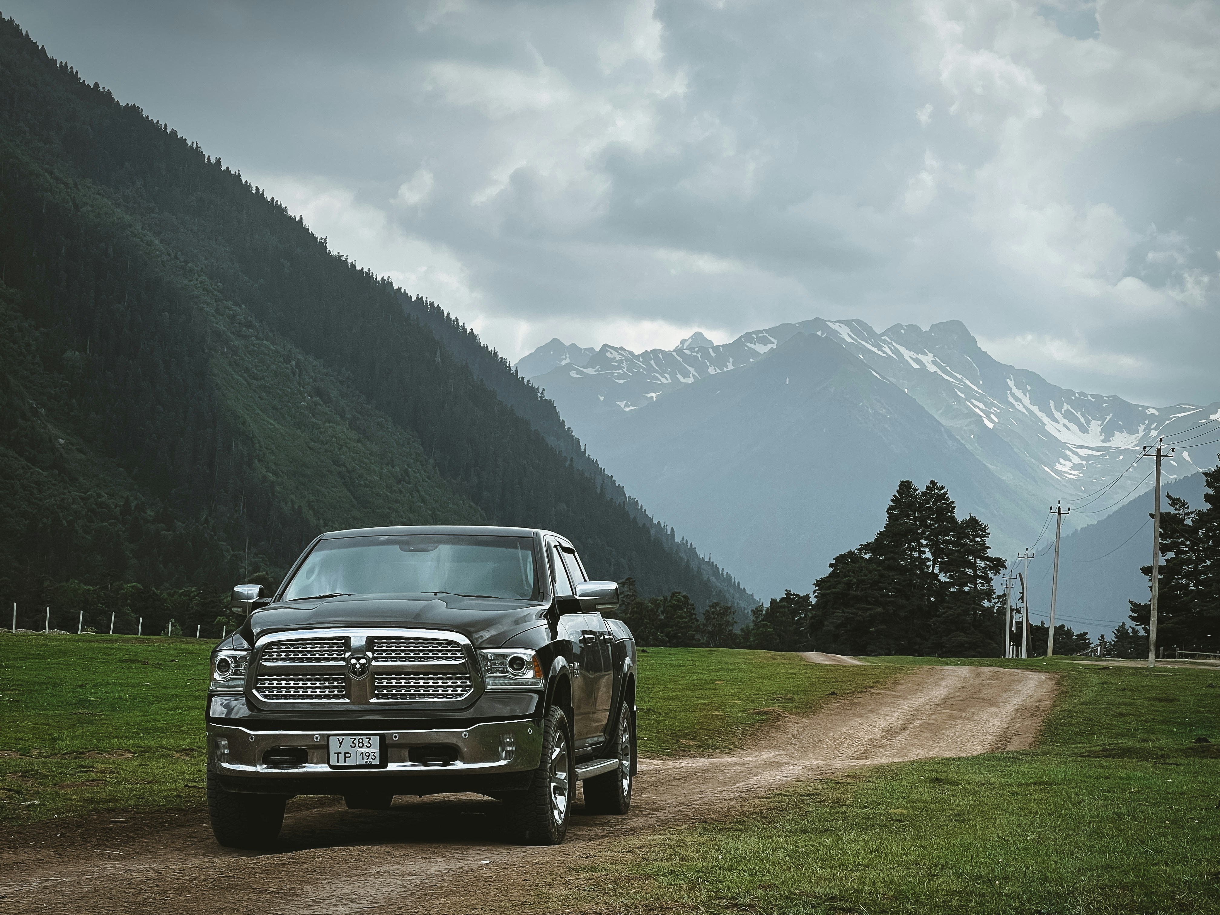 A truck drives on a dirt road with mountain views.