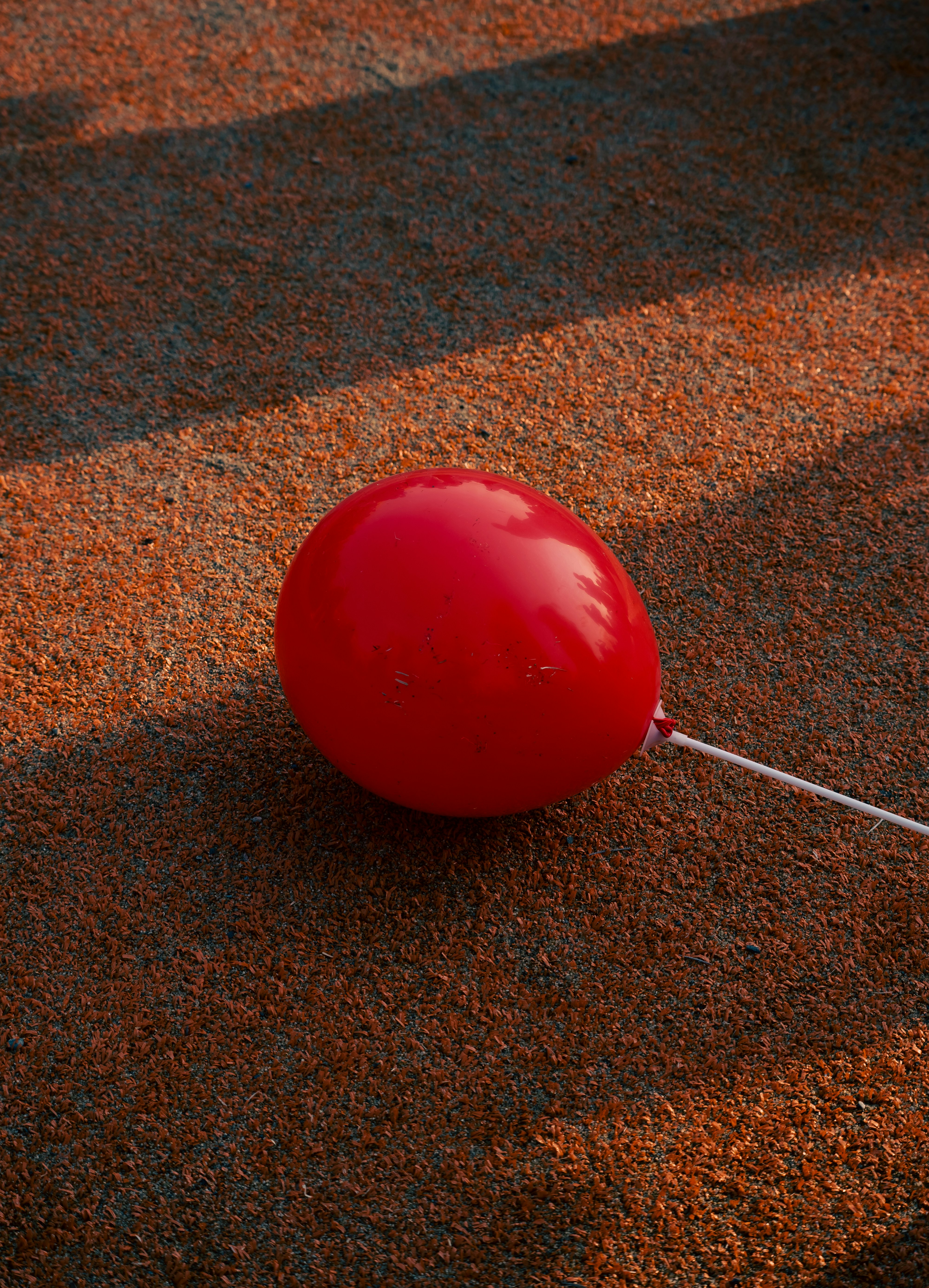 A red balloon sits on a rough, brown surface.