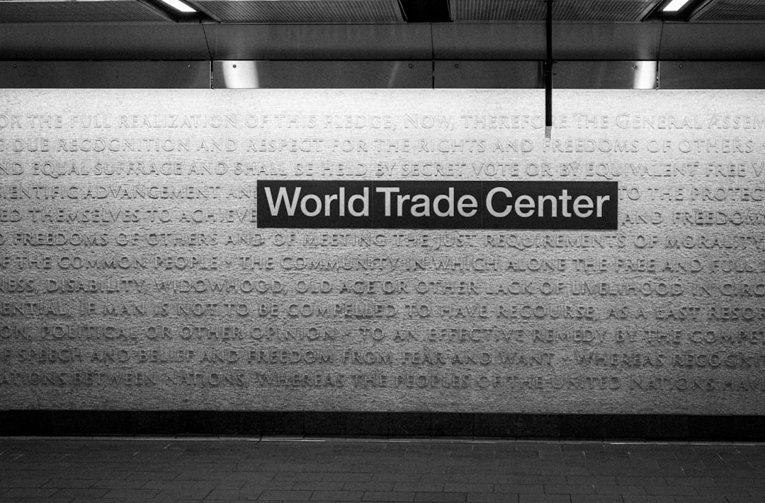 The world trade center sign hangs in a subway station., A marble mosaic wall installation titled CHORUS by Ann Hamilton at the WTC Cortlandt subway station in New York City. The 4,350-square-foot artwork integrates text from the U.S. Declaration of Independence and the 1948 Universal Declaration of Human Rights. Located within the World Trade Center Transportation Hub, the piece forms a monochromatic, tactile surface that merges art with architecture. It serves as a quiet but powerful reminder of national and universal values embedded in a space shaped by resilience and renewal.