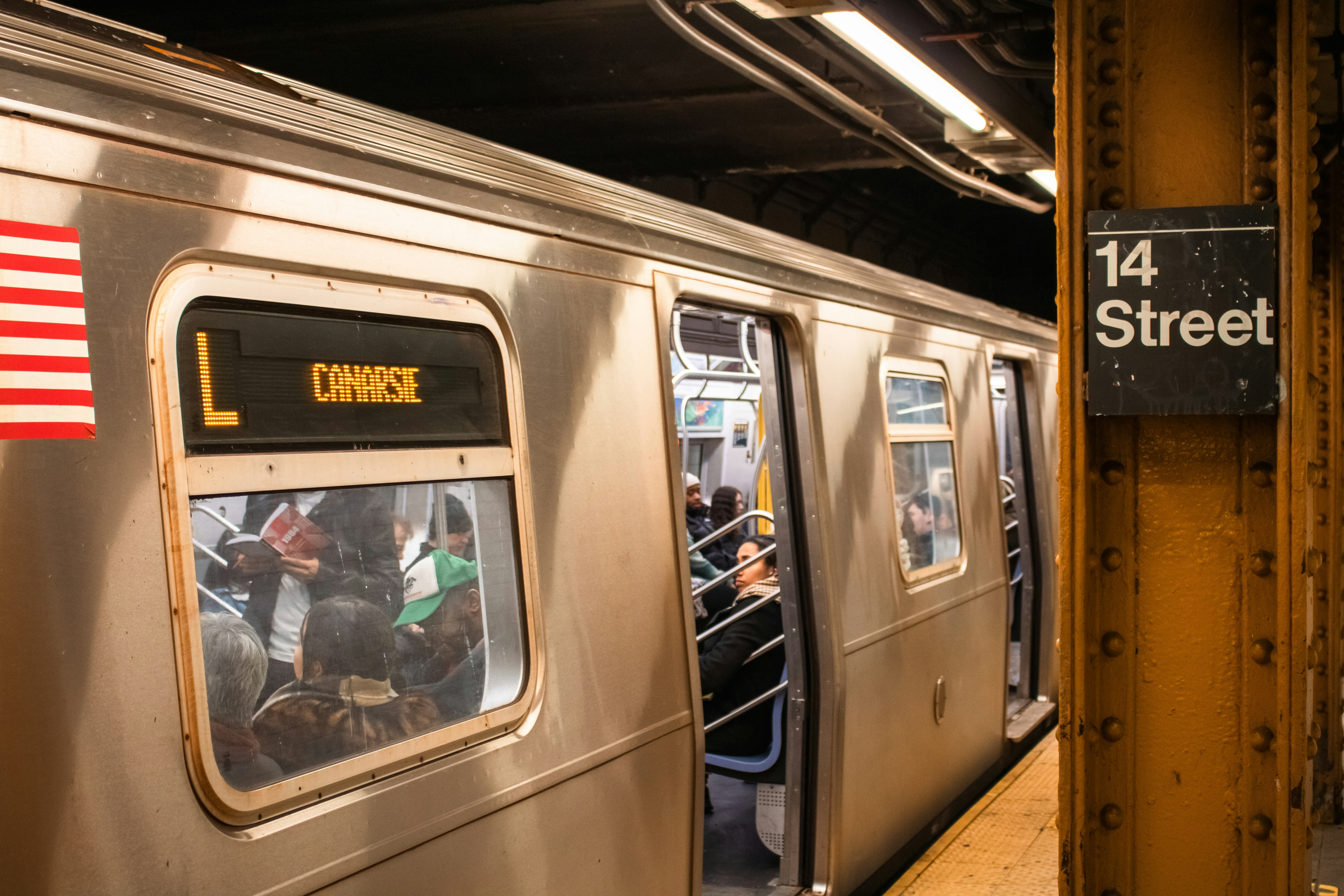 A subway train at the 14th street station., An L train is stopped at the 14th Street station in New York City. Most passengers have boarded, but the doors remain open for any last-minute entries. The image captures a paused moment in the subway’s daily rhythm, reflecting the flow of urban commuting within the MTA system. Set in a busy Manhattan station, it highlights the balance between movement and waiting in NYC’s public transportation network.