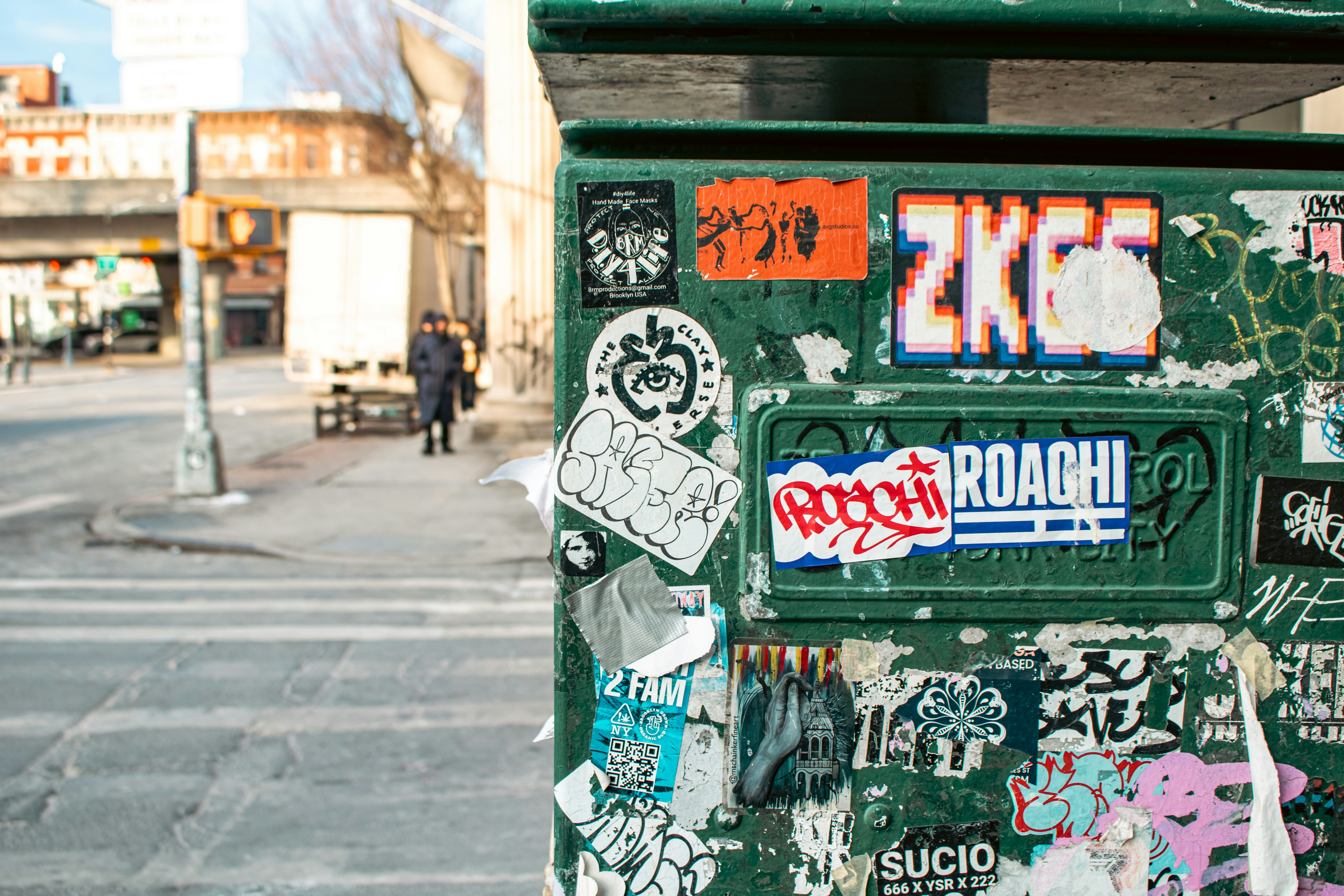 Sticker-covered trash can in a city environment.