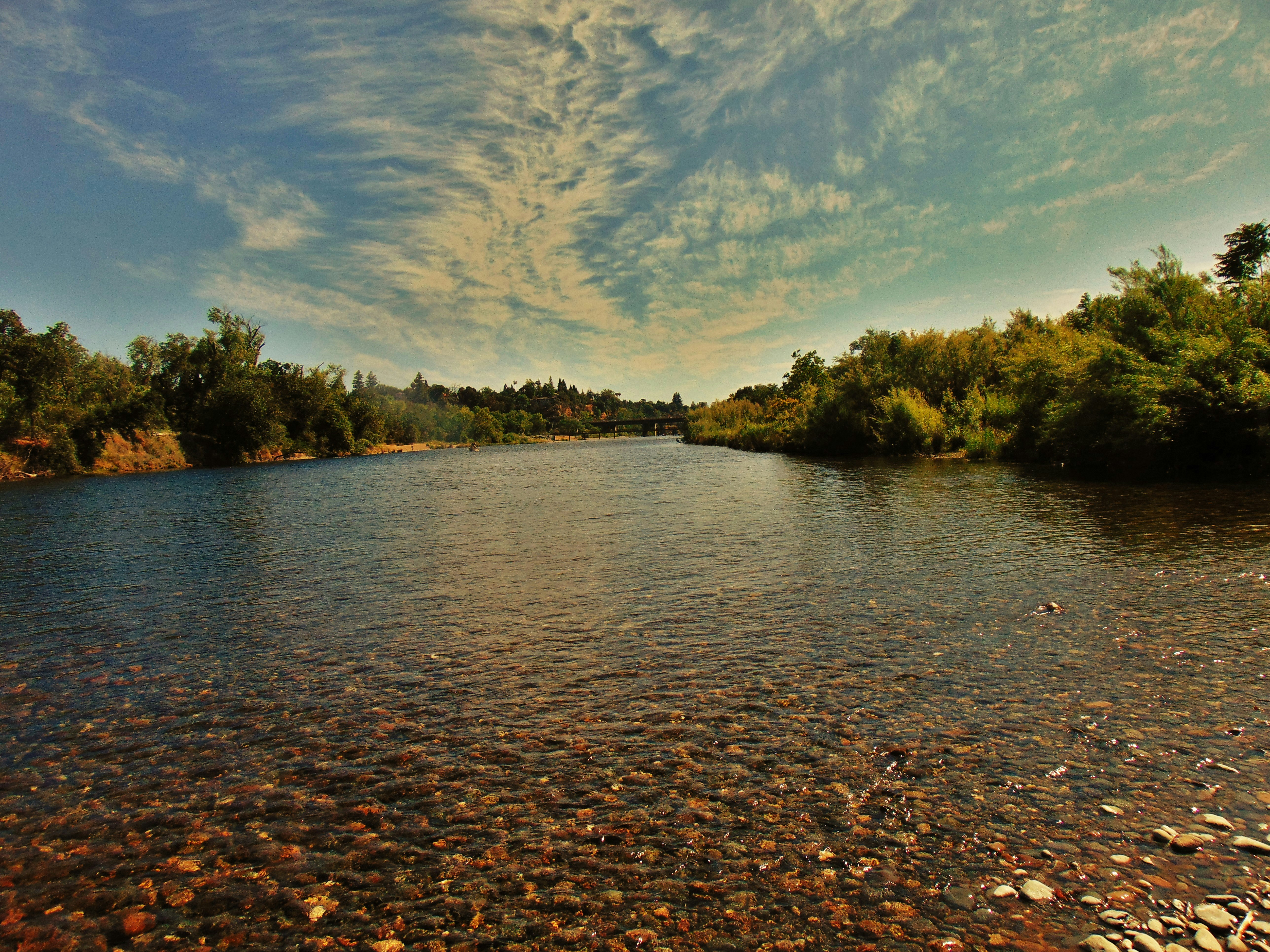 A serene river flows under a cloudy blue sky.