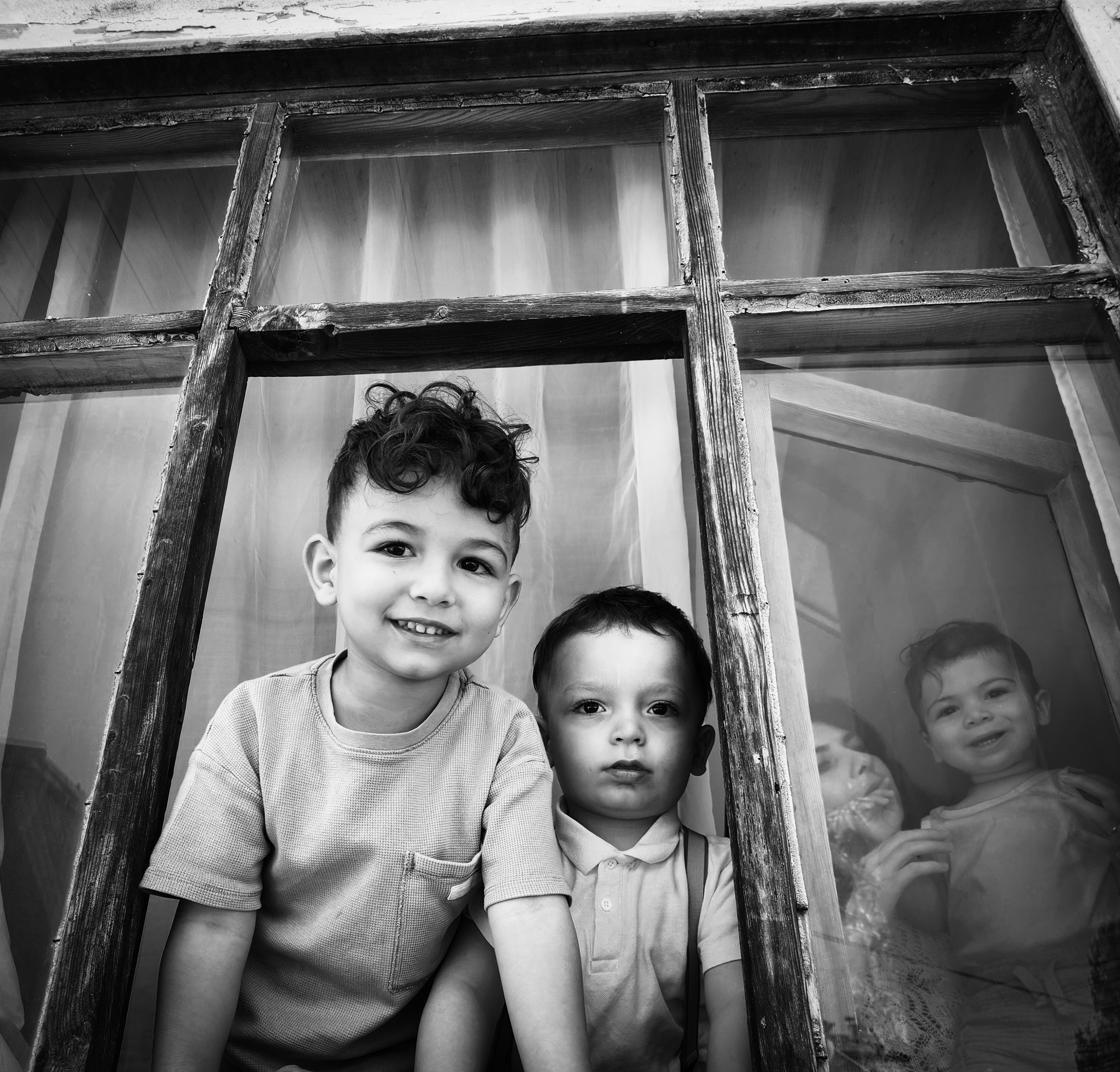 Two young boys and reflection in a window frame.