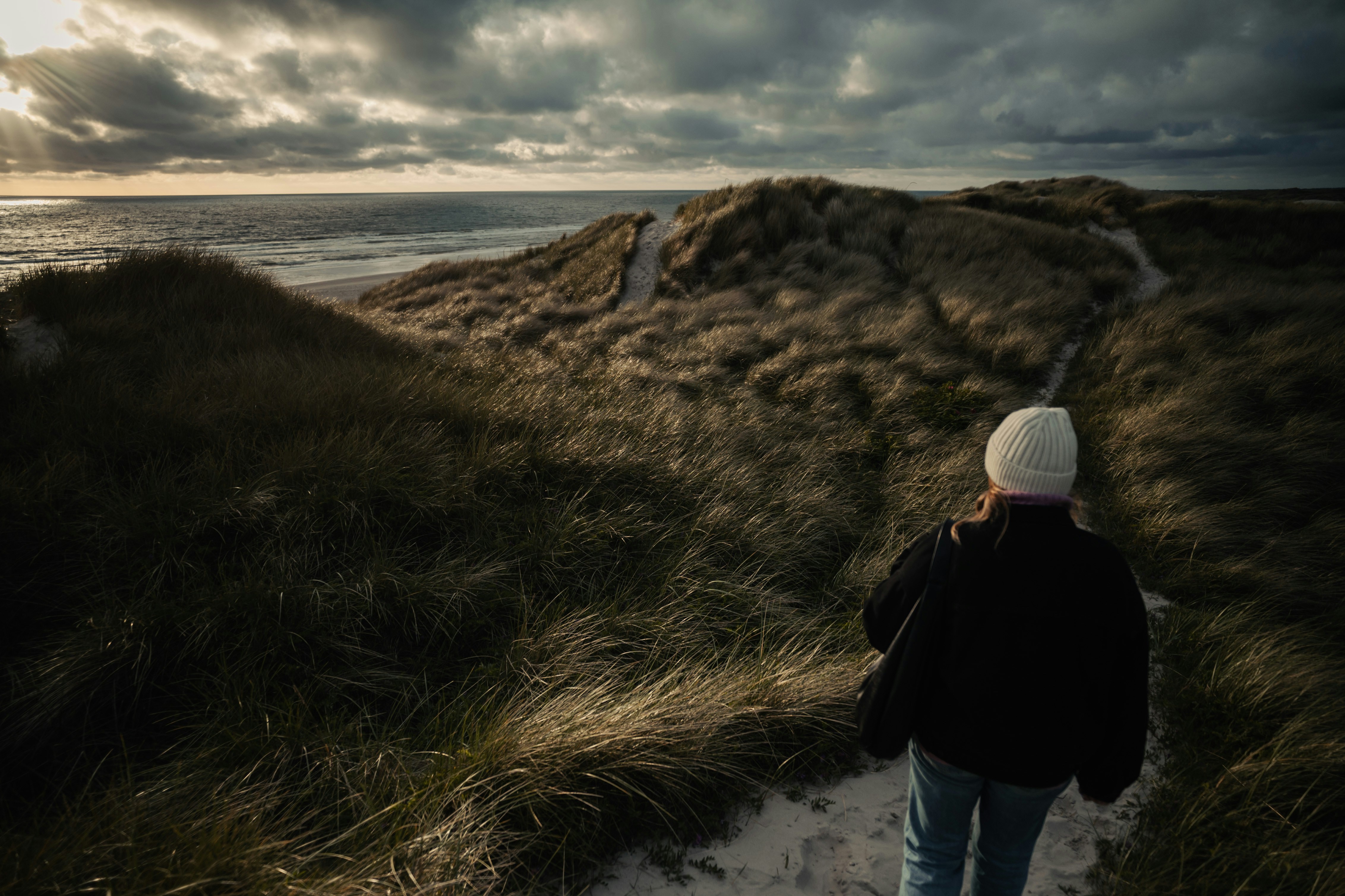 A person walks towards the ocean at sunset.