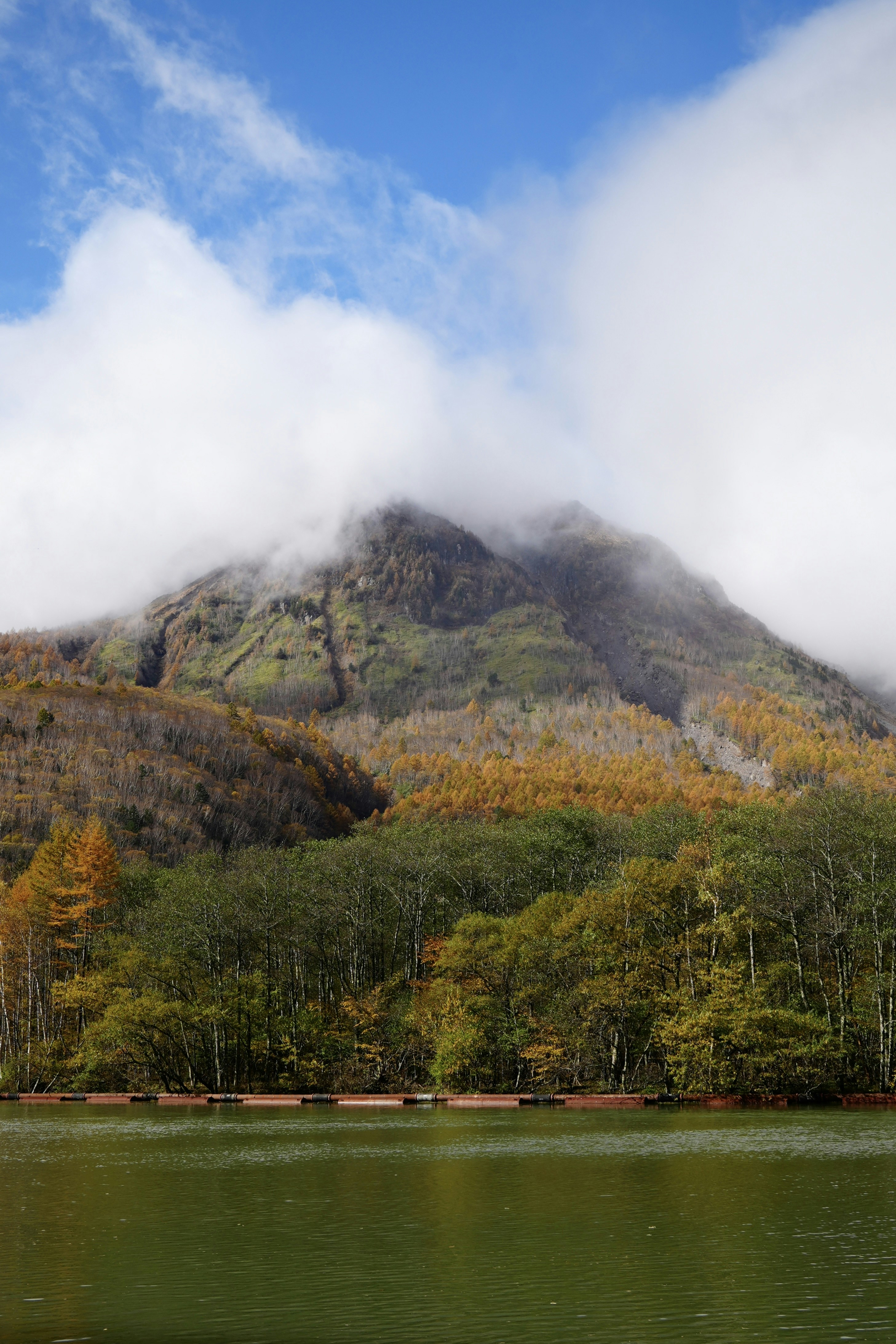 A mountain peak shrouded in clouds overlooks a lake.