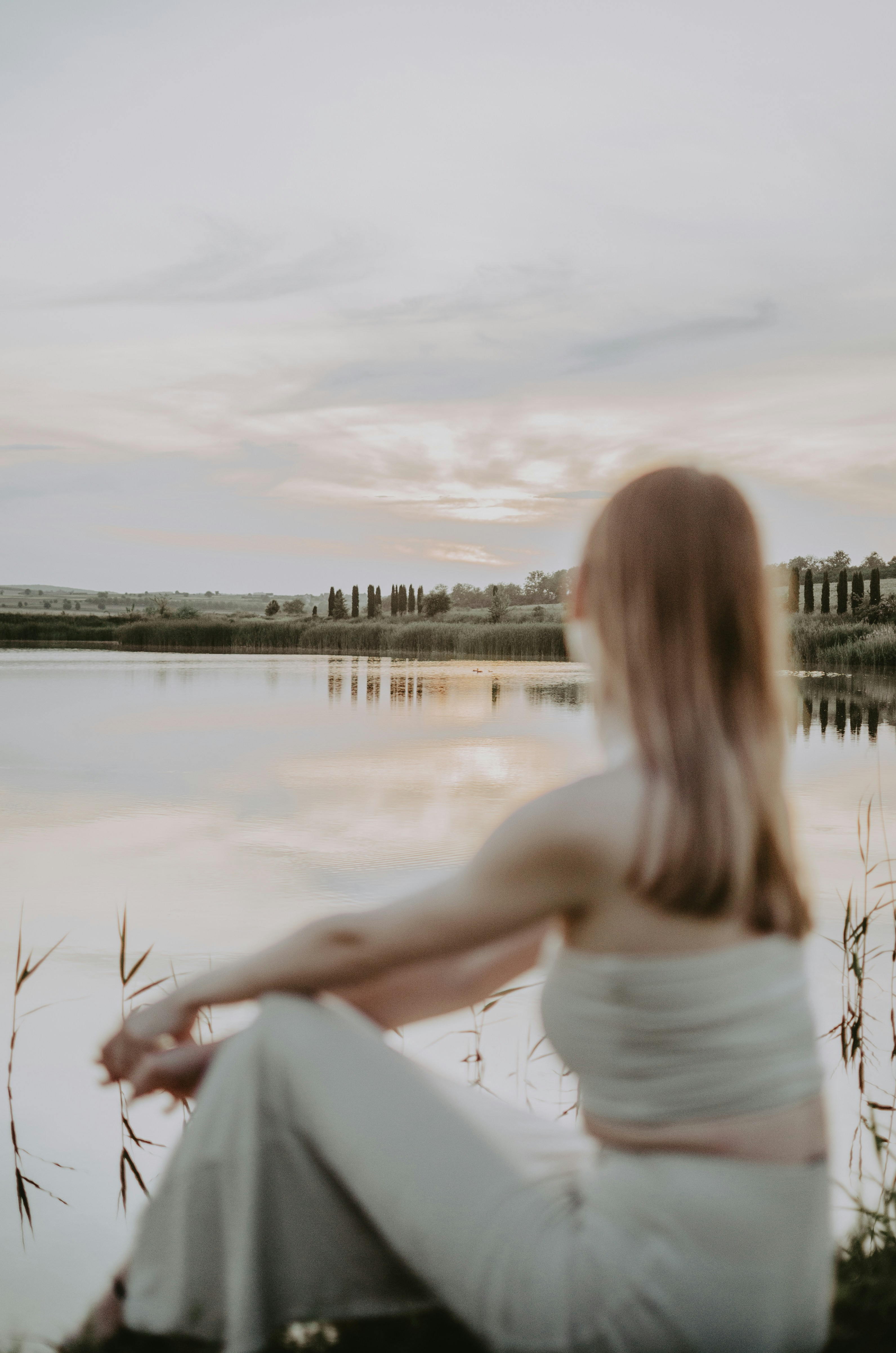 Woman sitting by the lake, enjoying the sunset.