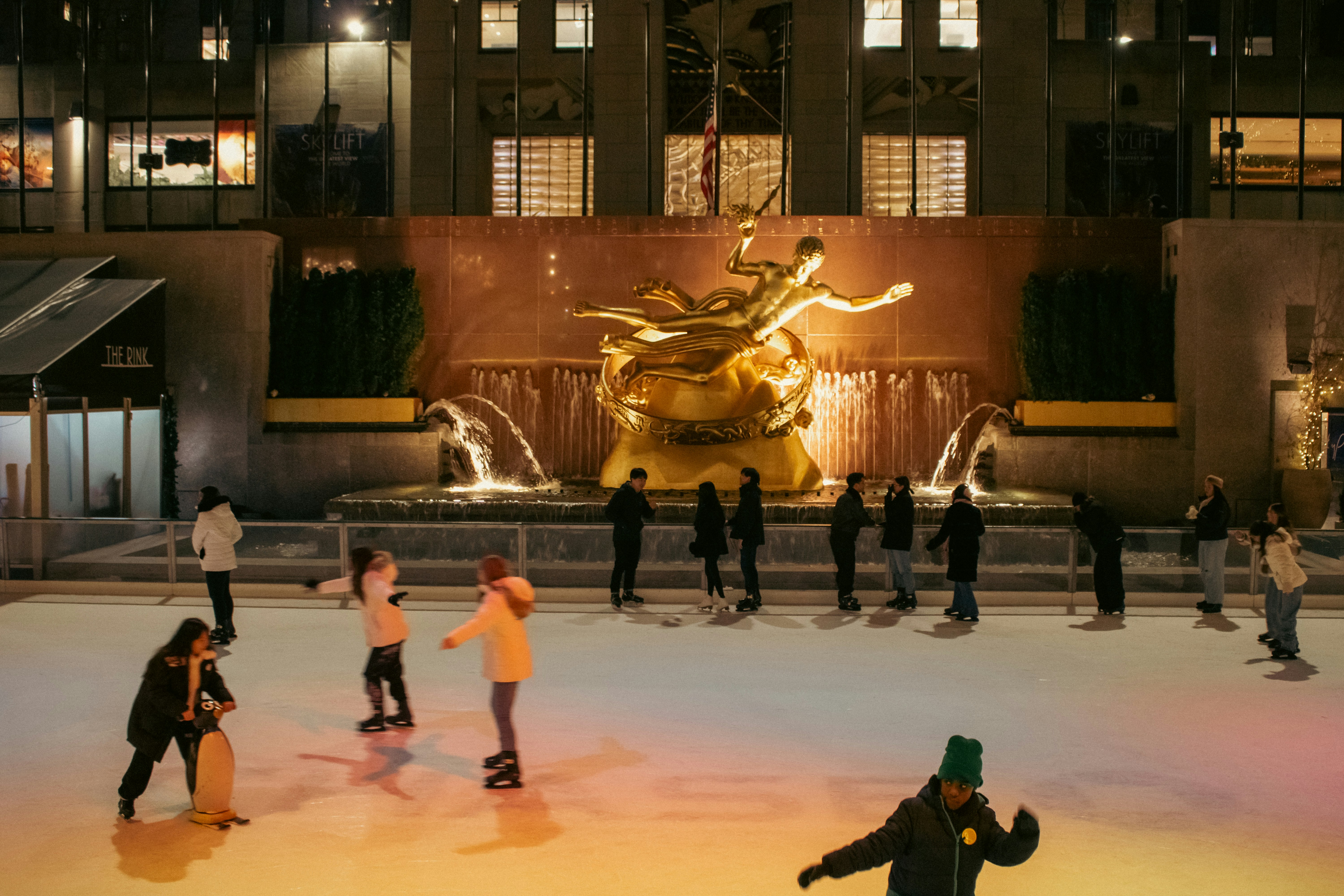 People ice skate in front of a golden fountain.