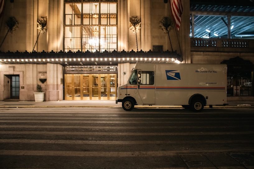 A usps truck sits outside a grand building.