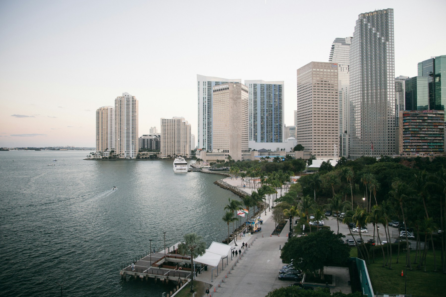 Miami high-rise skyline beside a waterfront promenade and palm trees.