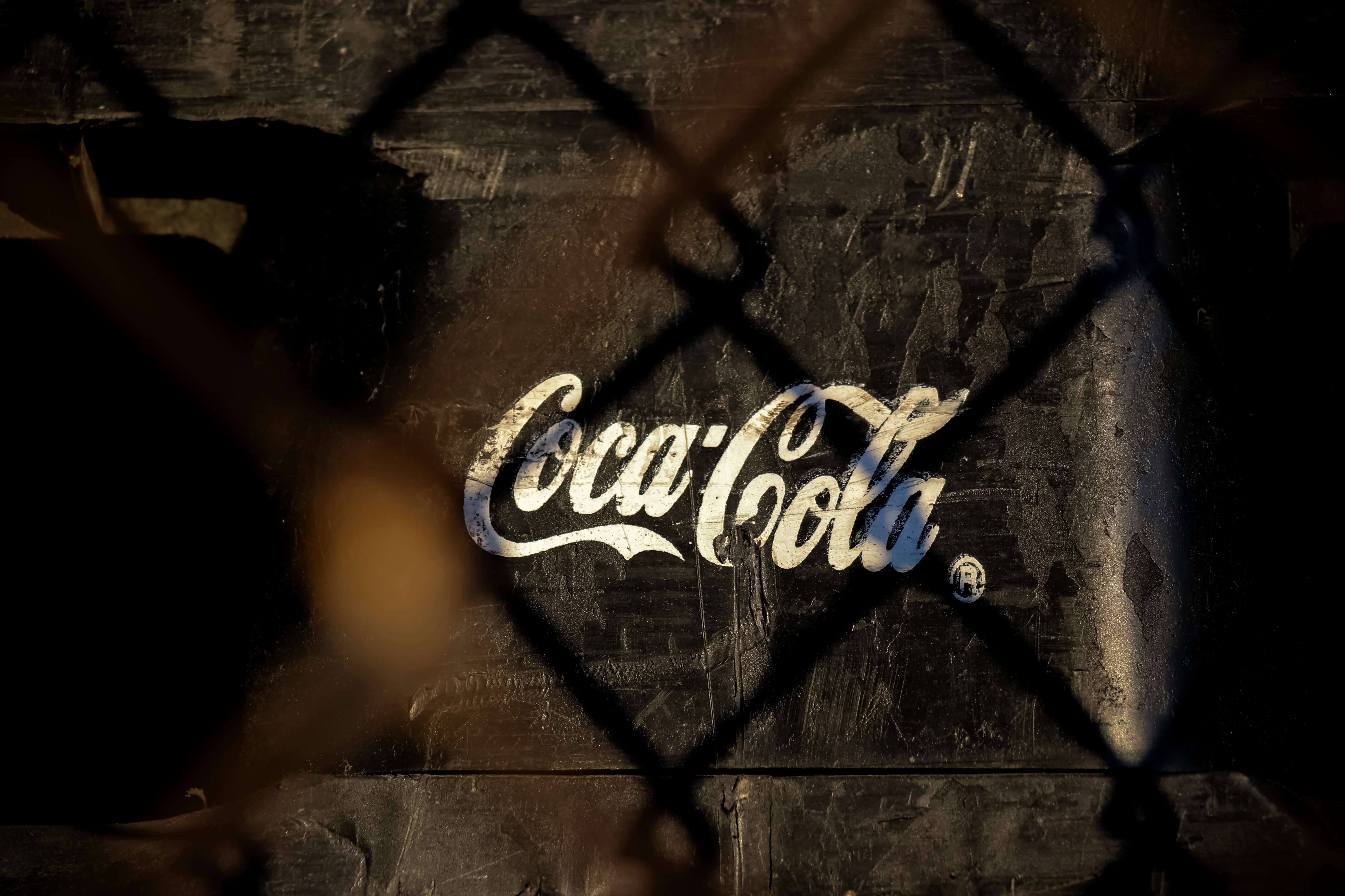 Coca-cola logo is seen through a chain link fence.