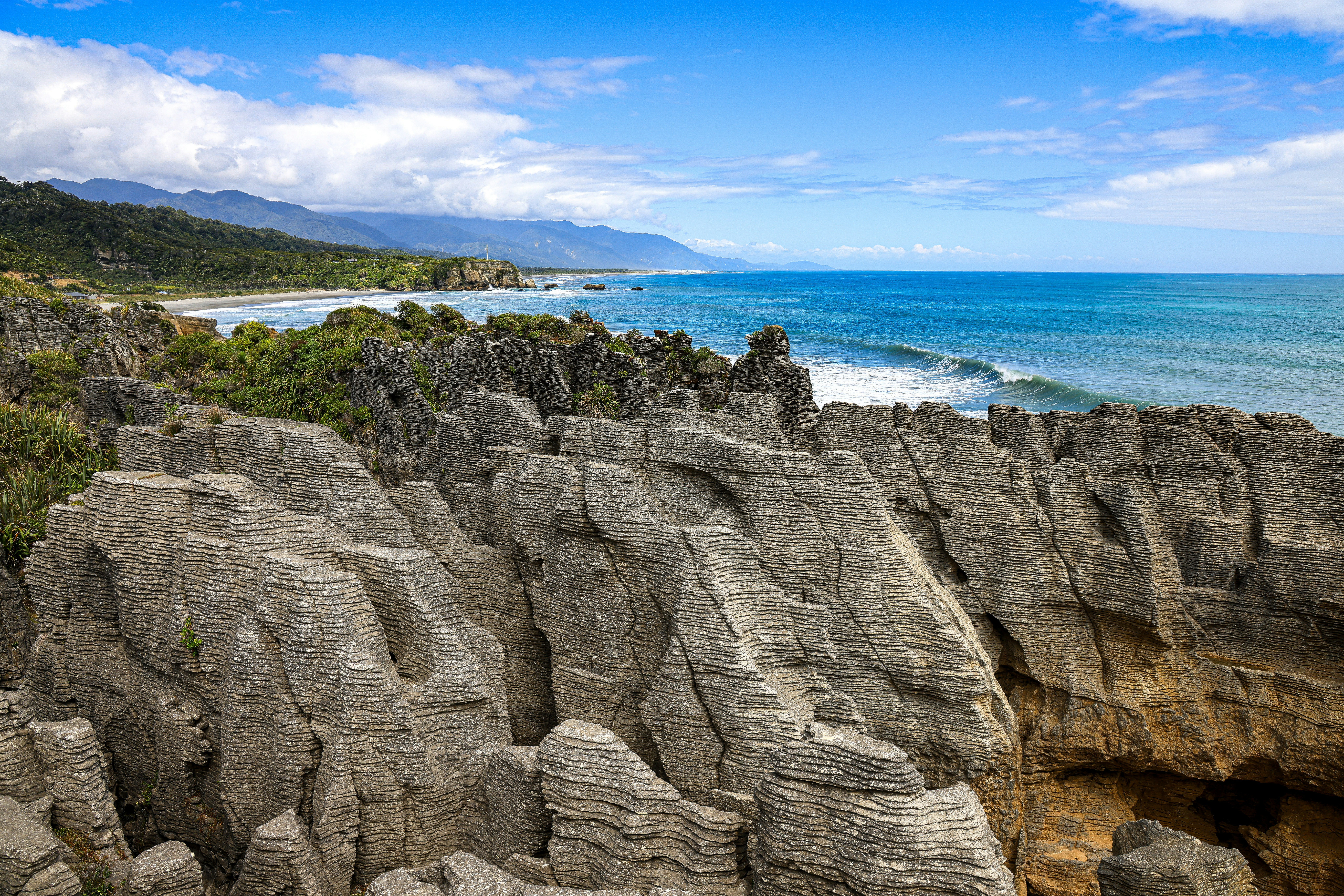Punakaiki to Hokitika: Pancake Rocks, Lake Brunner and Gorge – Coastal rock formations meet the ocean under a blue sky