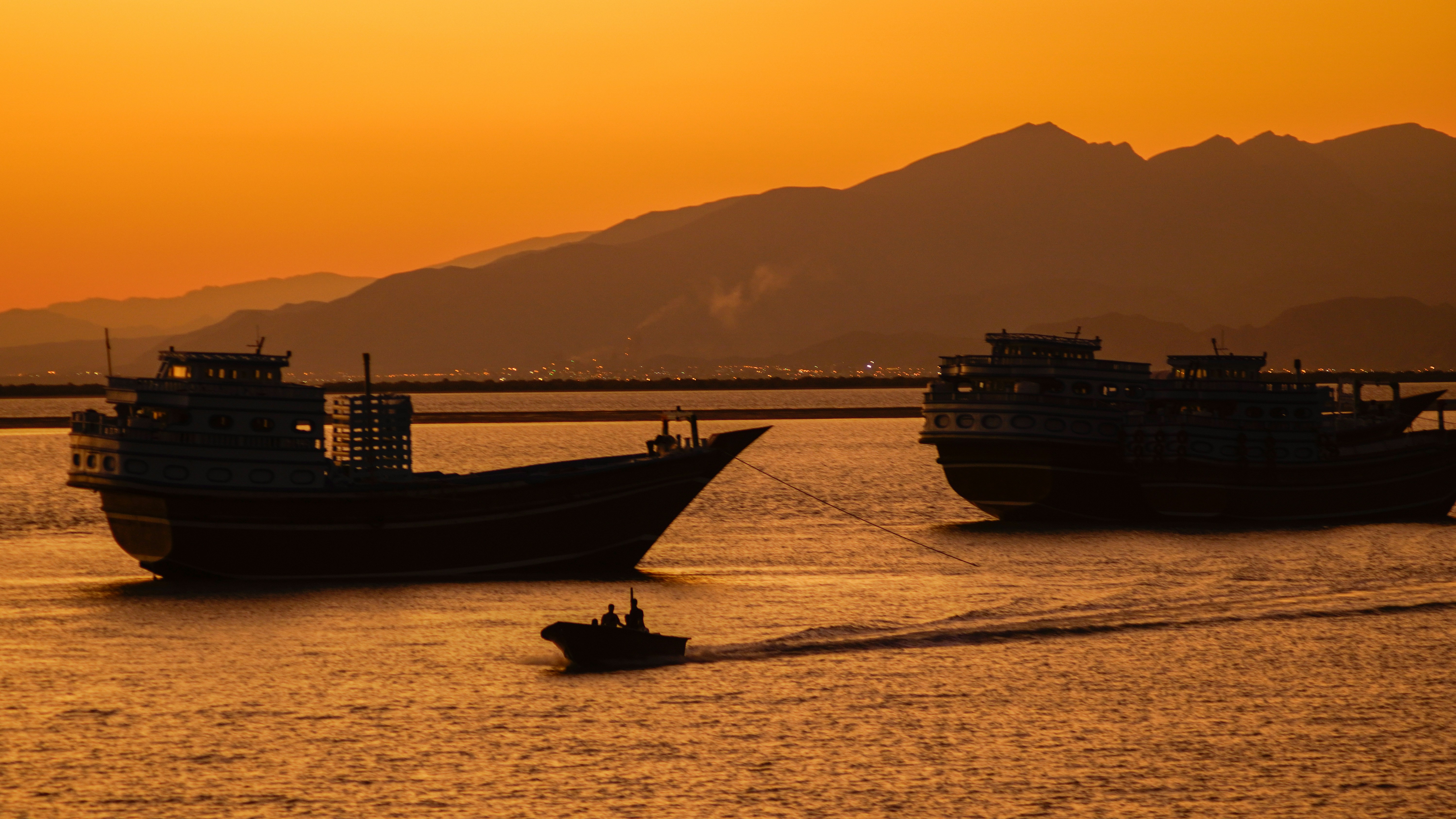 Boats sail at sunset with mountains in the background.