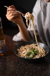 Someone is eating pasta with a beer nearby.