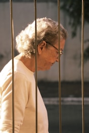 An elderly woman stands behind a metal fence.