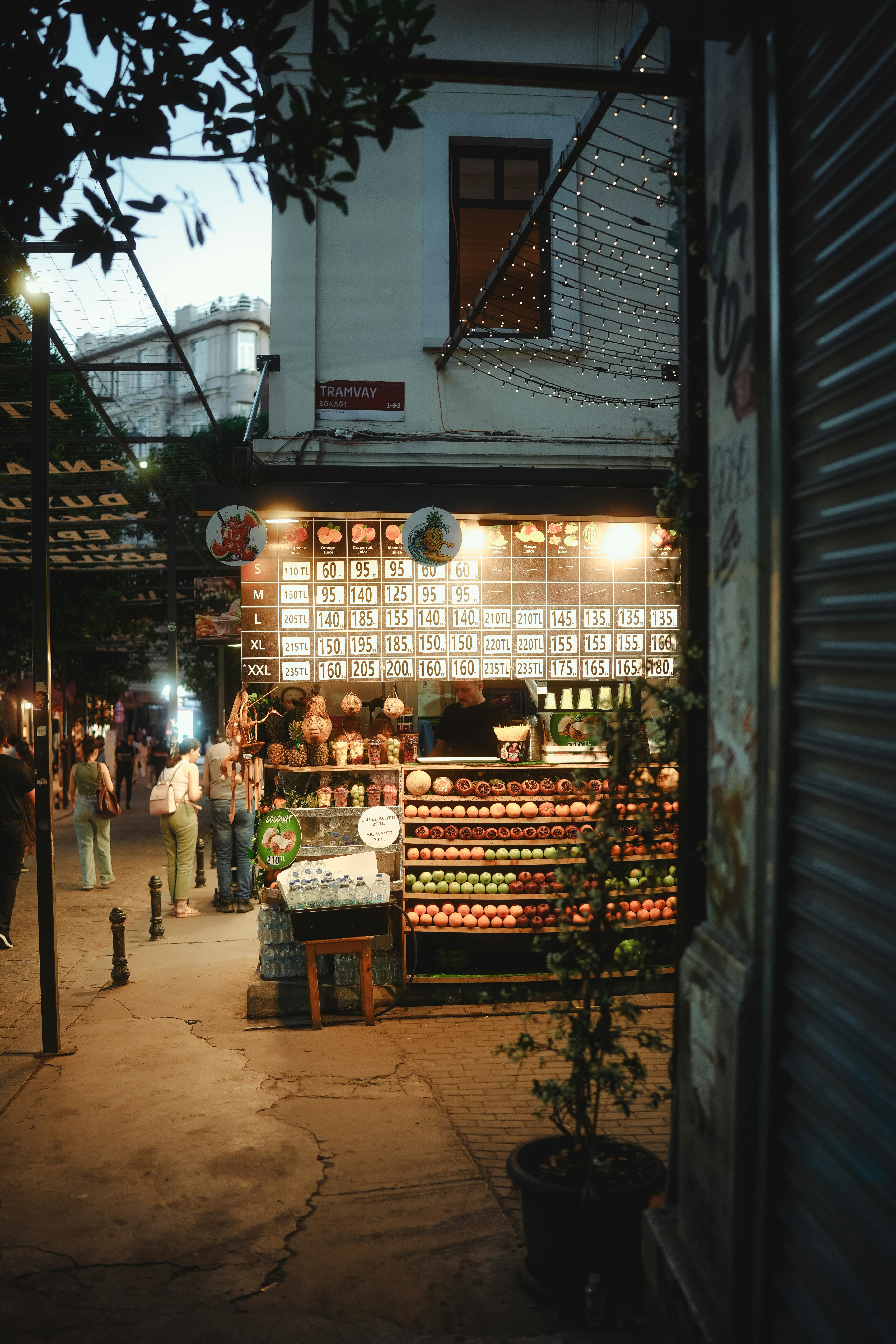 A fruit stand in an alleyway is lit up.