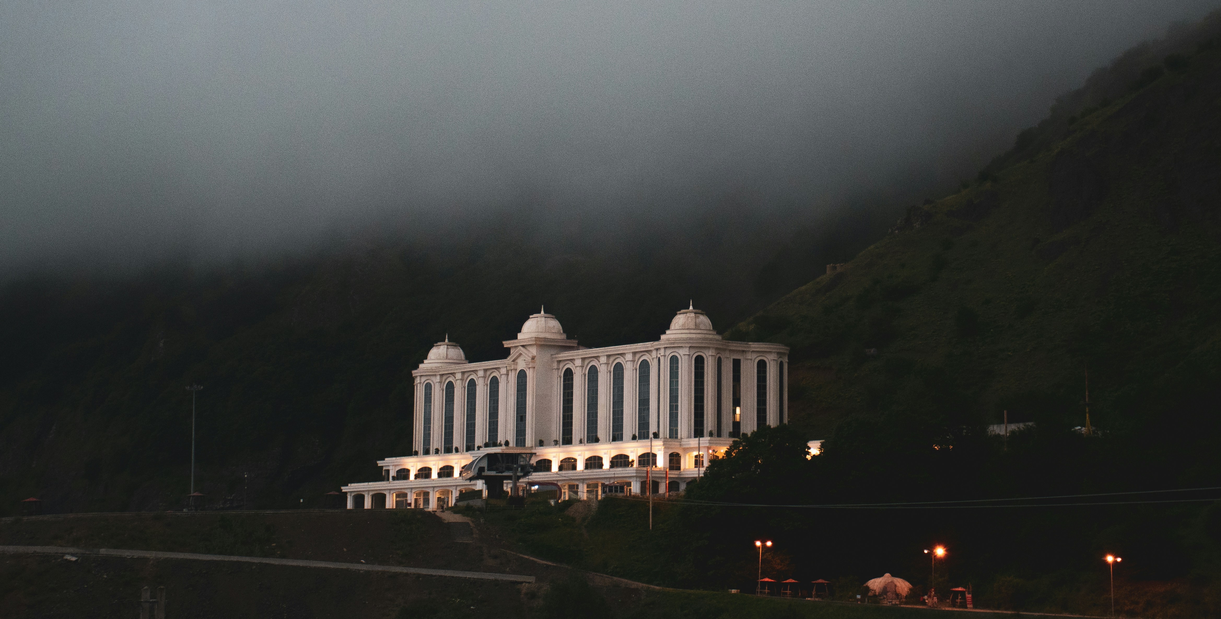 A majestic white mansion emerges from the fog in Heyran Pass, Gilan Province, Iran. Surrounded by dark mountain silhouettes and lit softly from within, this scene captures the quiet mystery of northern Iran's mountain roads.