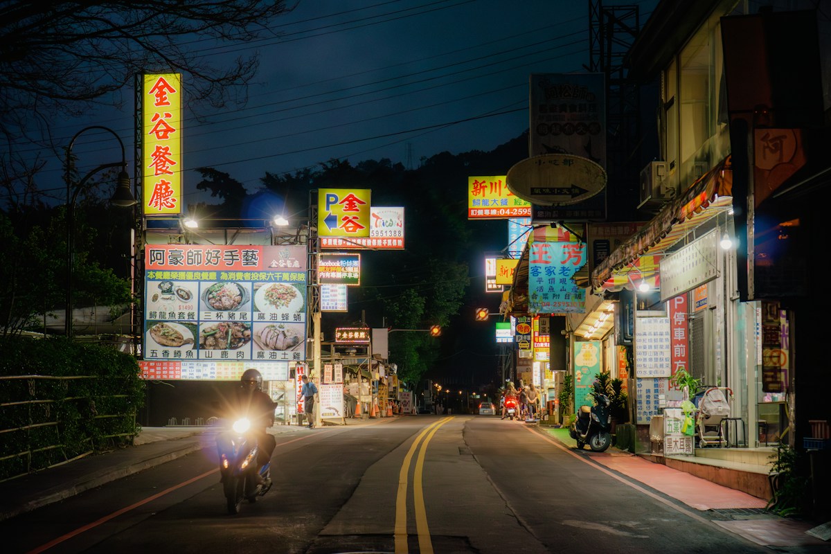 台灣山區小鎮的夜晚道路，一輛機車開著大燈行駛