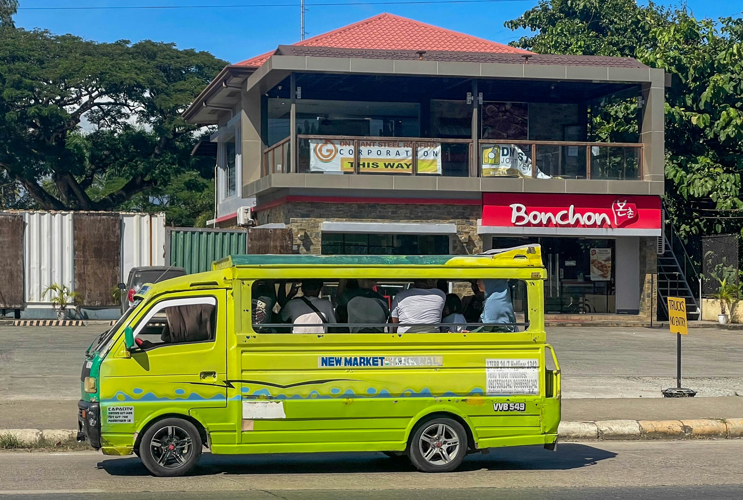 A yellow jeepney travels past a bonchon restaurant.