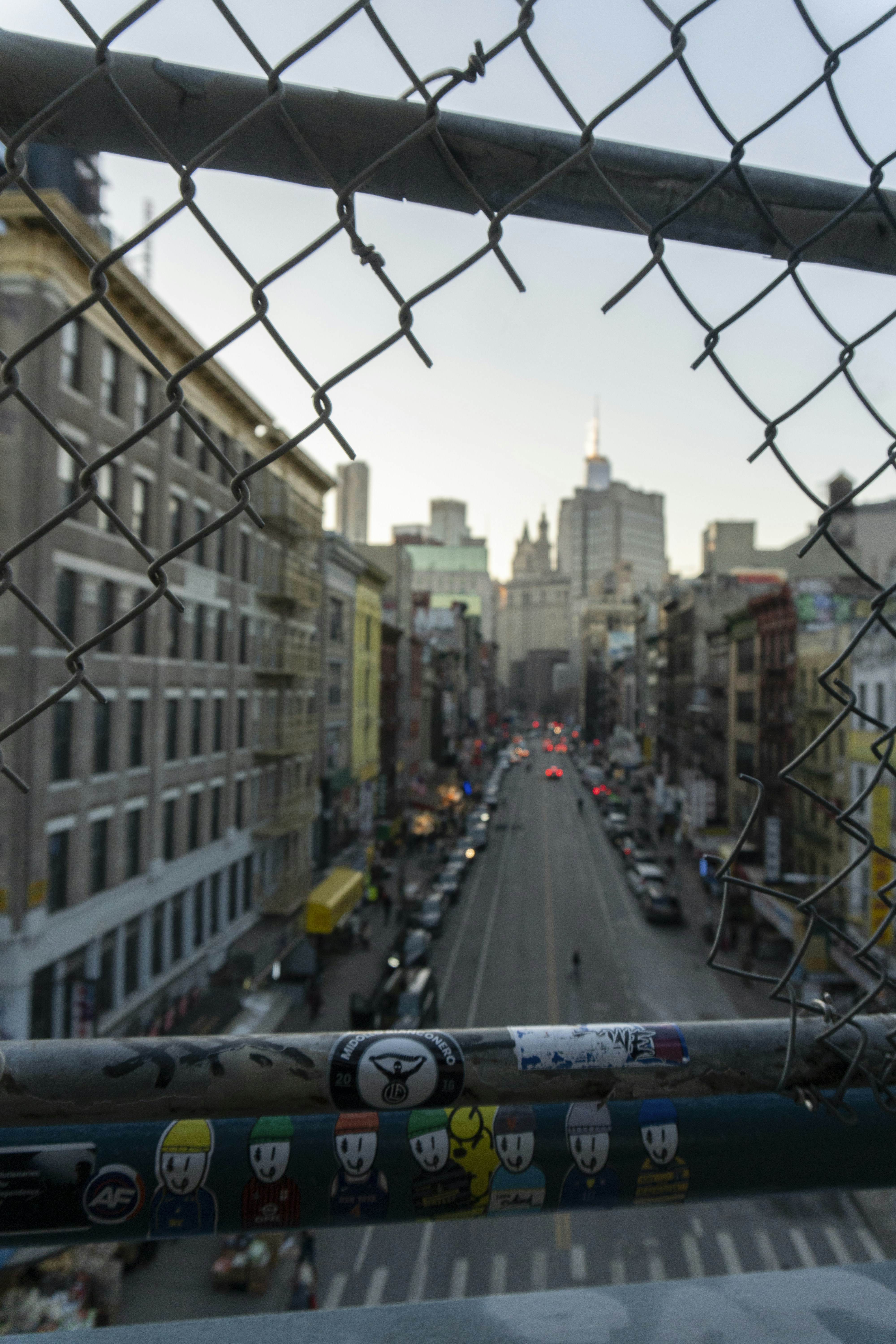 A city street is framed by a chain-link fence.