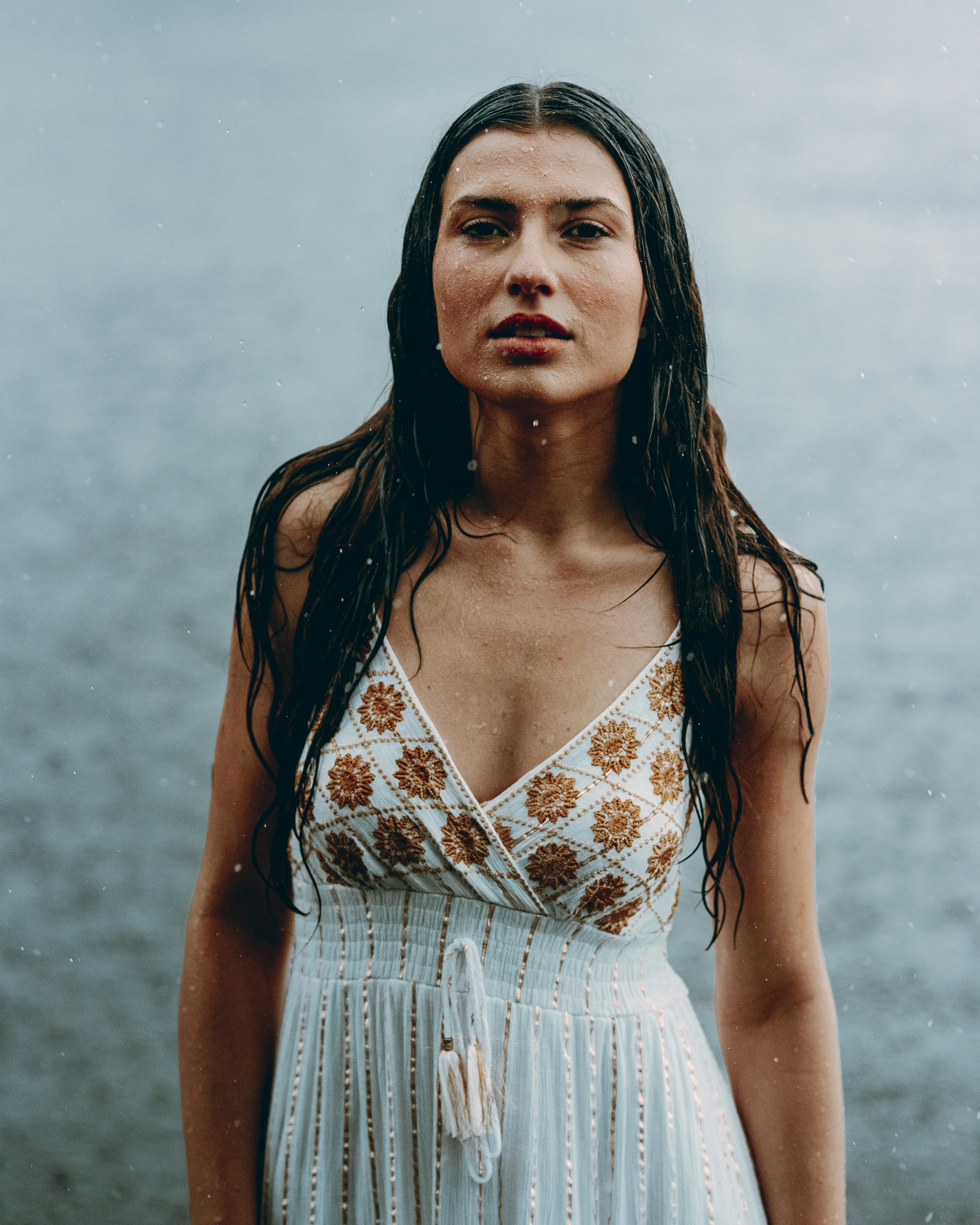 A woman stands in the rain, looking at the camera.