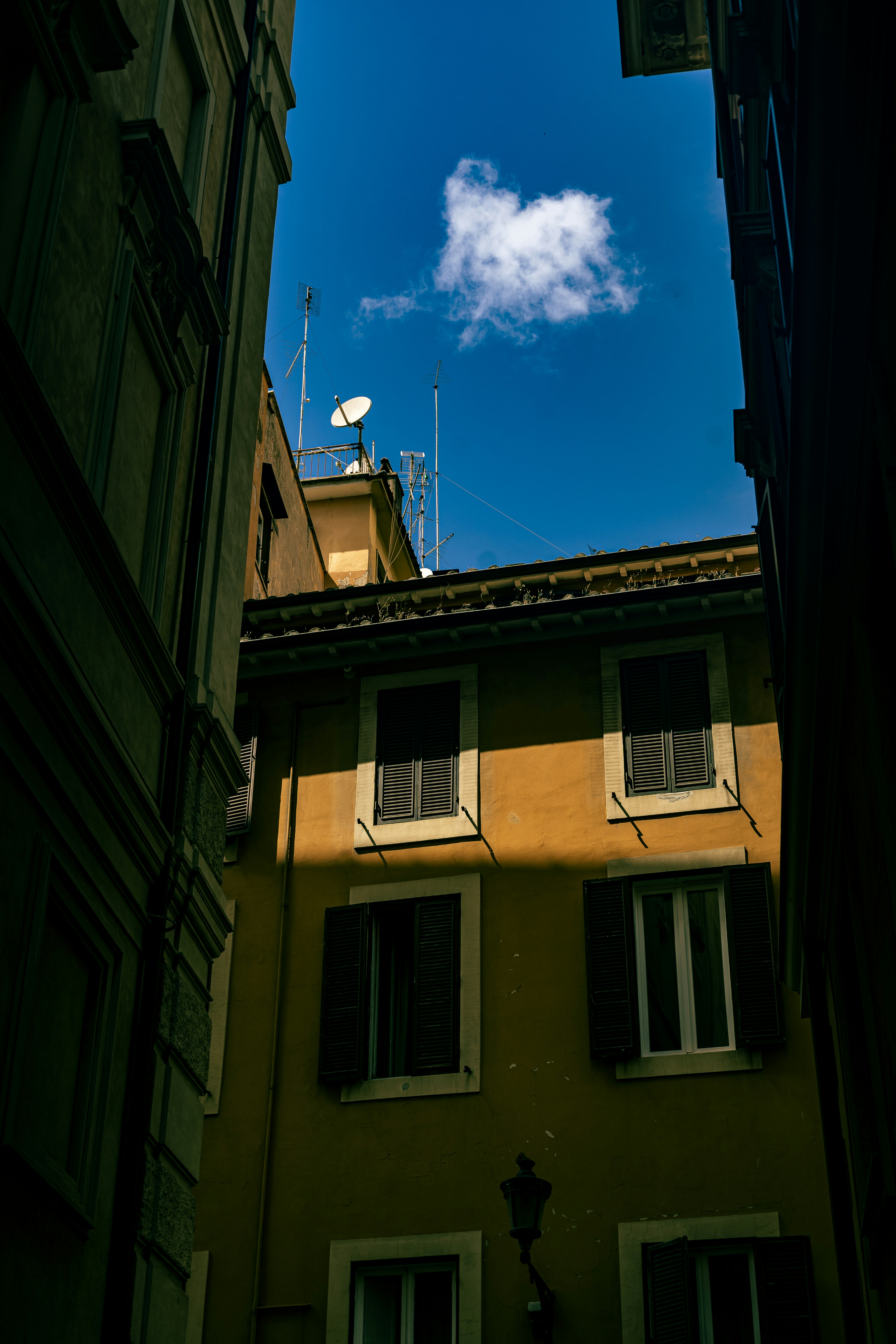 Buildings frame a bright blue sky and a puffy cloud.
