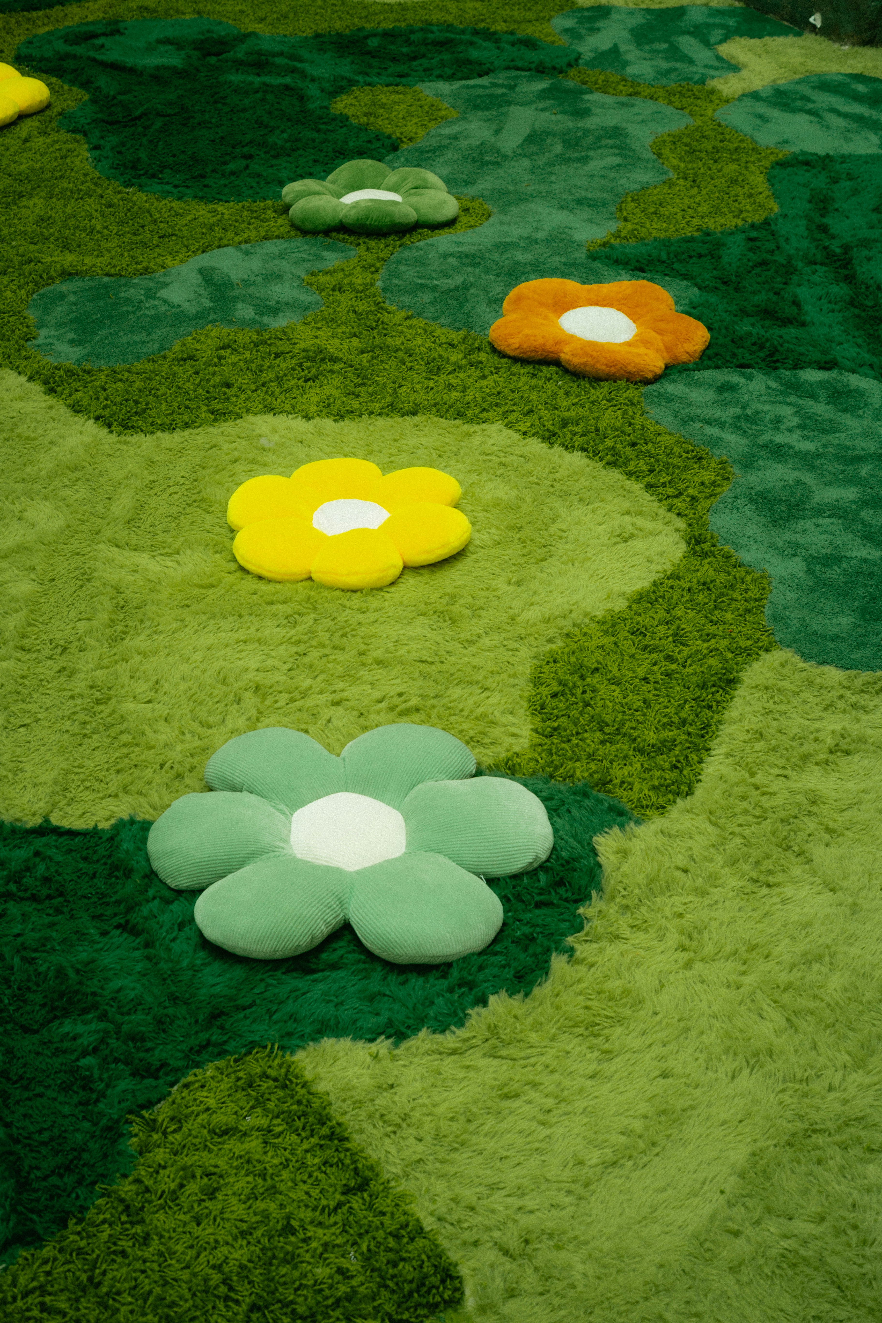 Bunte blumenförmige Kissen sind auf einem grünen Teppich arrangiert.