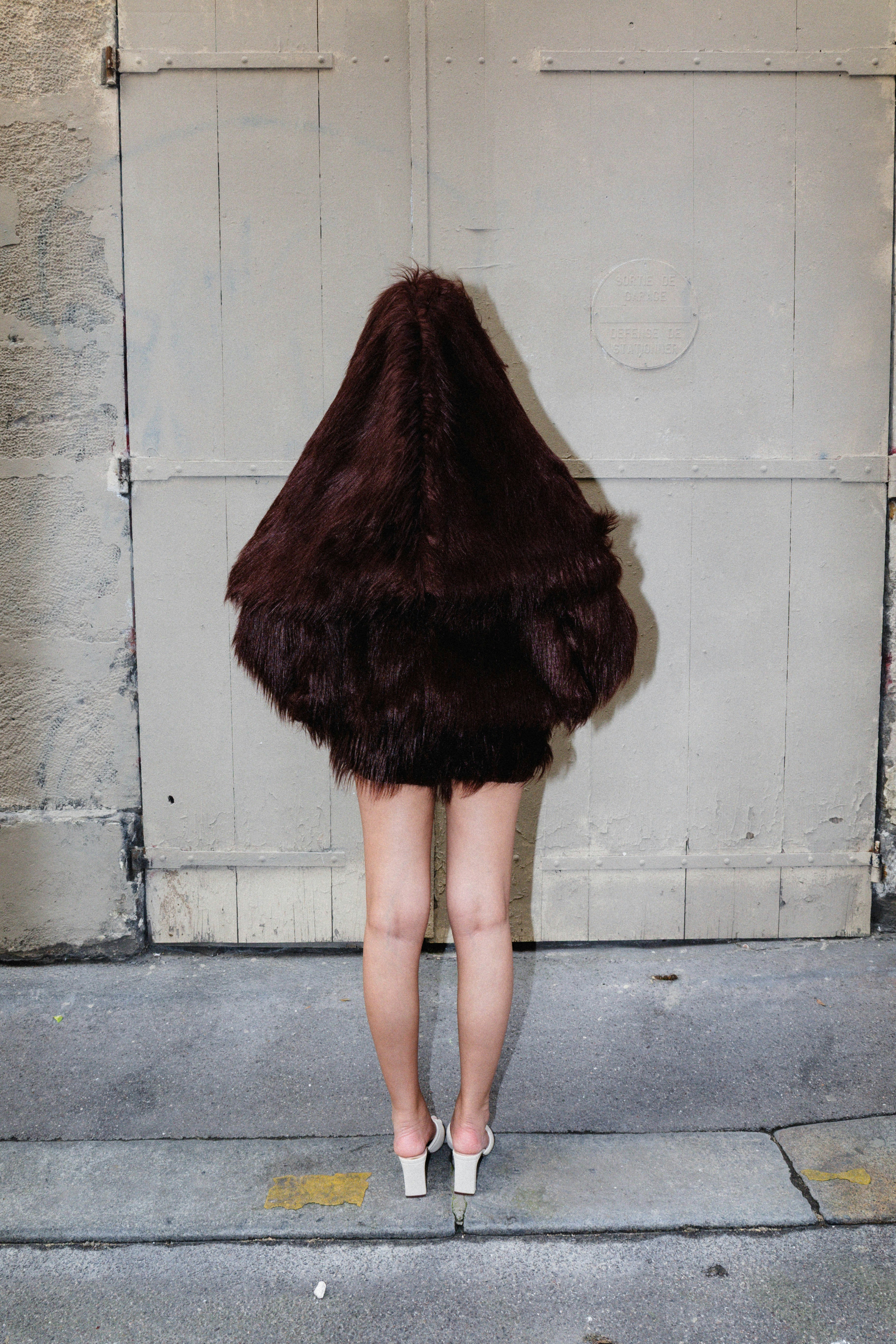 Person covered in hair stands before a door.