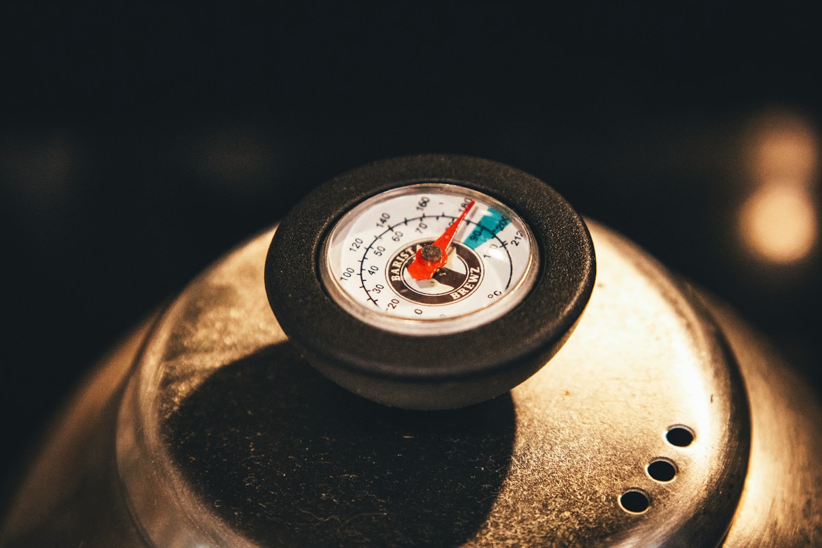 Analoges Rundthermometer mit rotem Zeiger und Celsius-Skala, Nahaufnahme auf einem Metallgefäss in warmem Licht