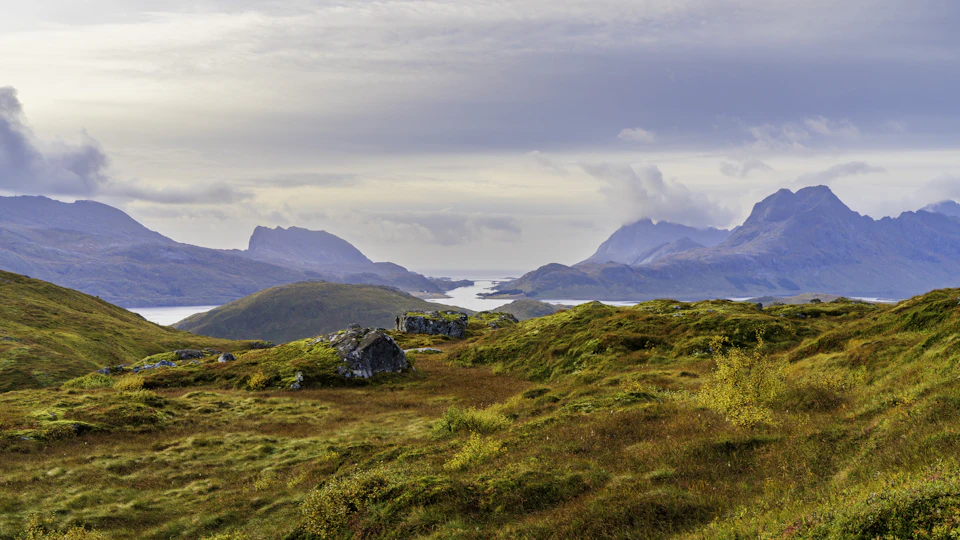 Serene landscape with rocky outcropping, valley, and distant mountains under overcast sky