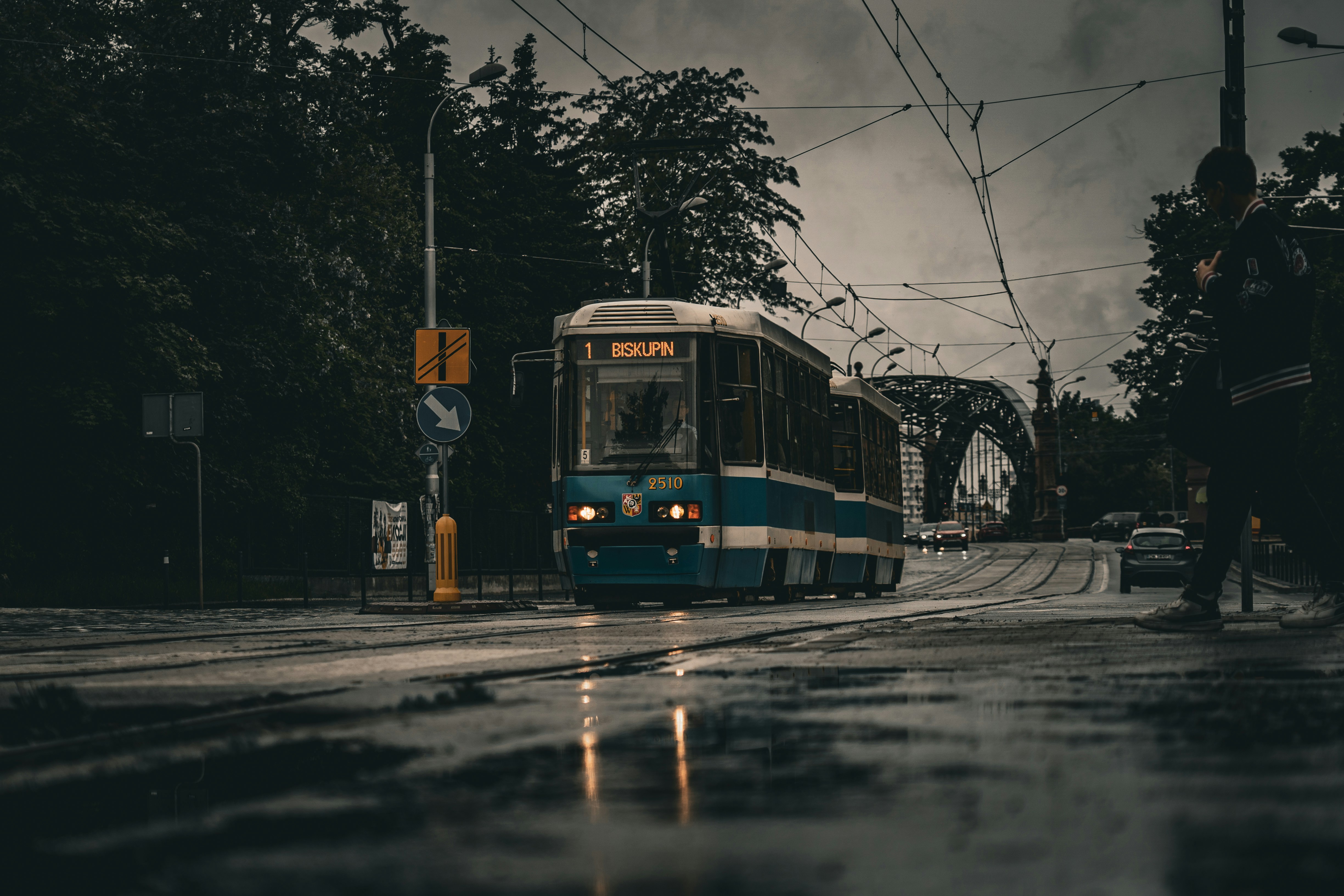 A blue tram rides down a wet city street.