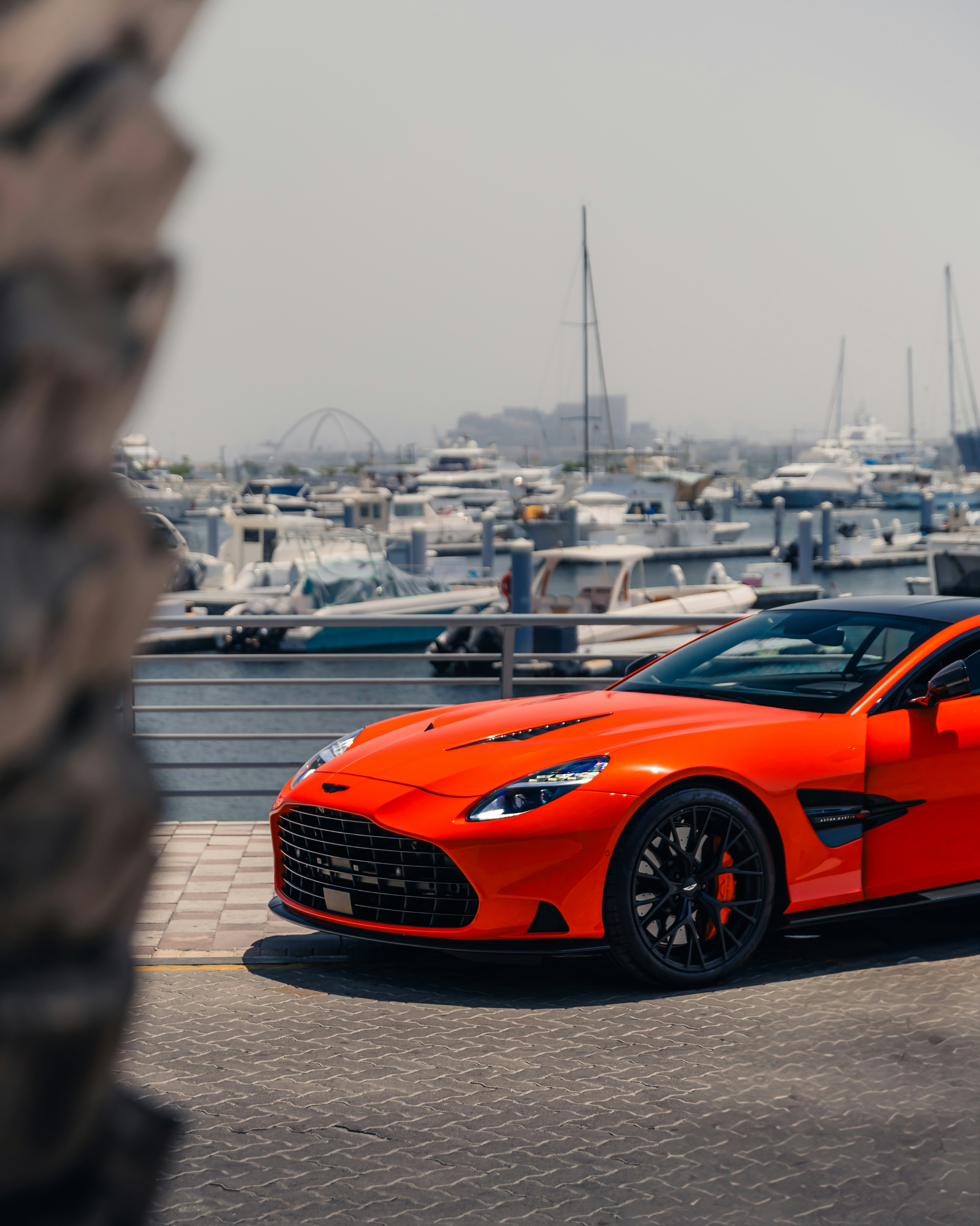 An orange sports car is parked by the marina.