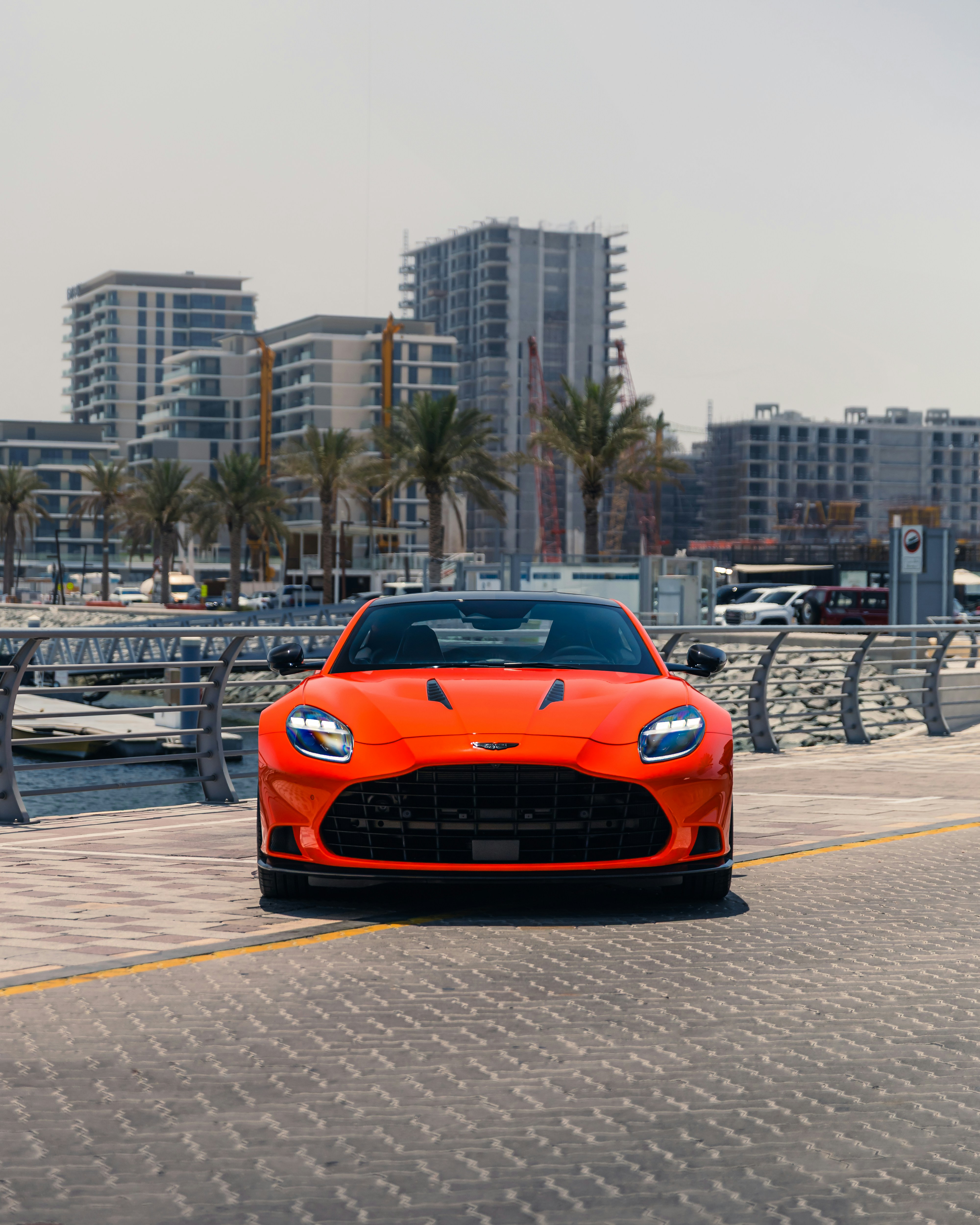 A sleek, orange sports car sits by the water.