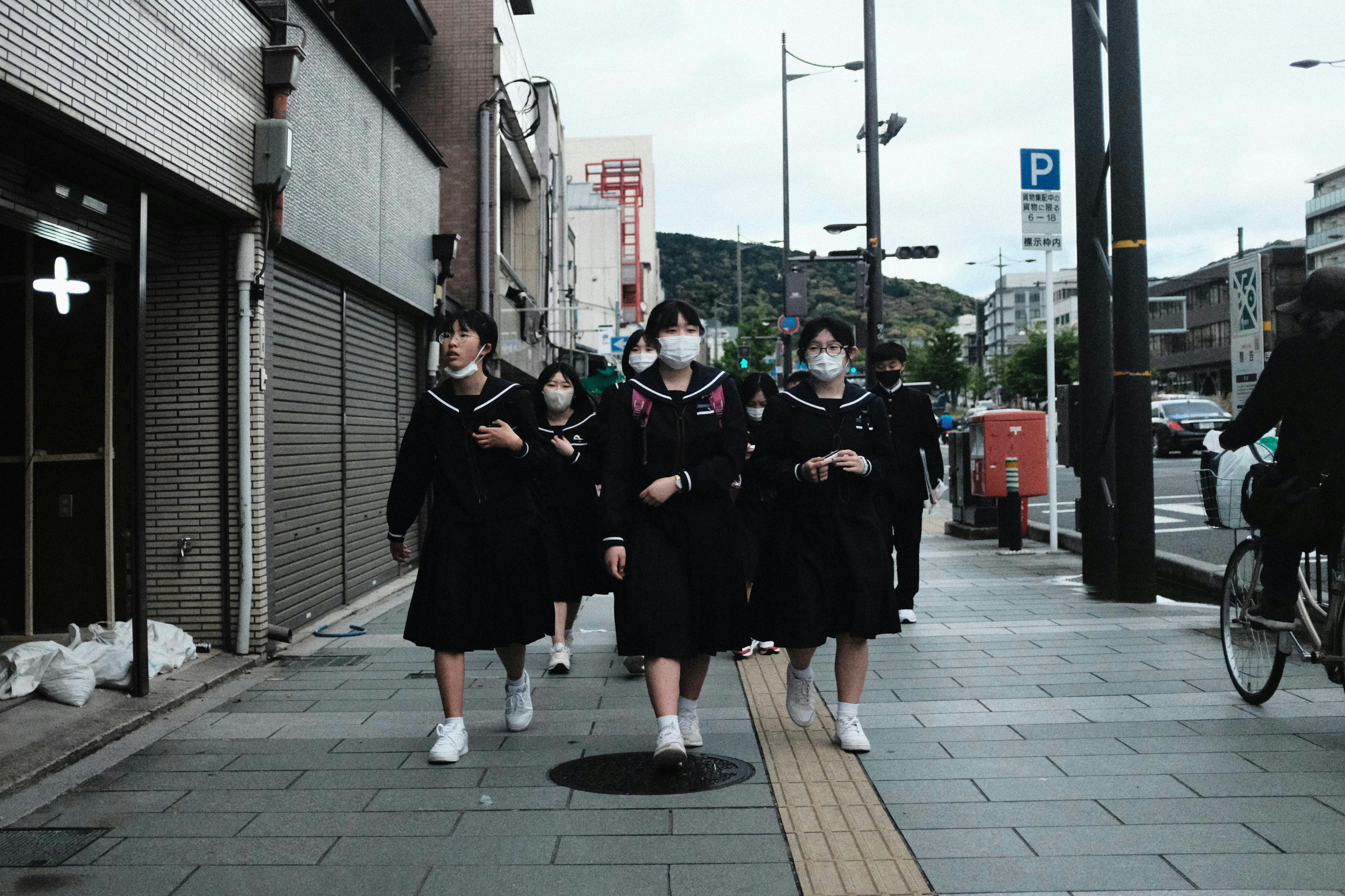 Schoolgirls wearing masks walk down a city street