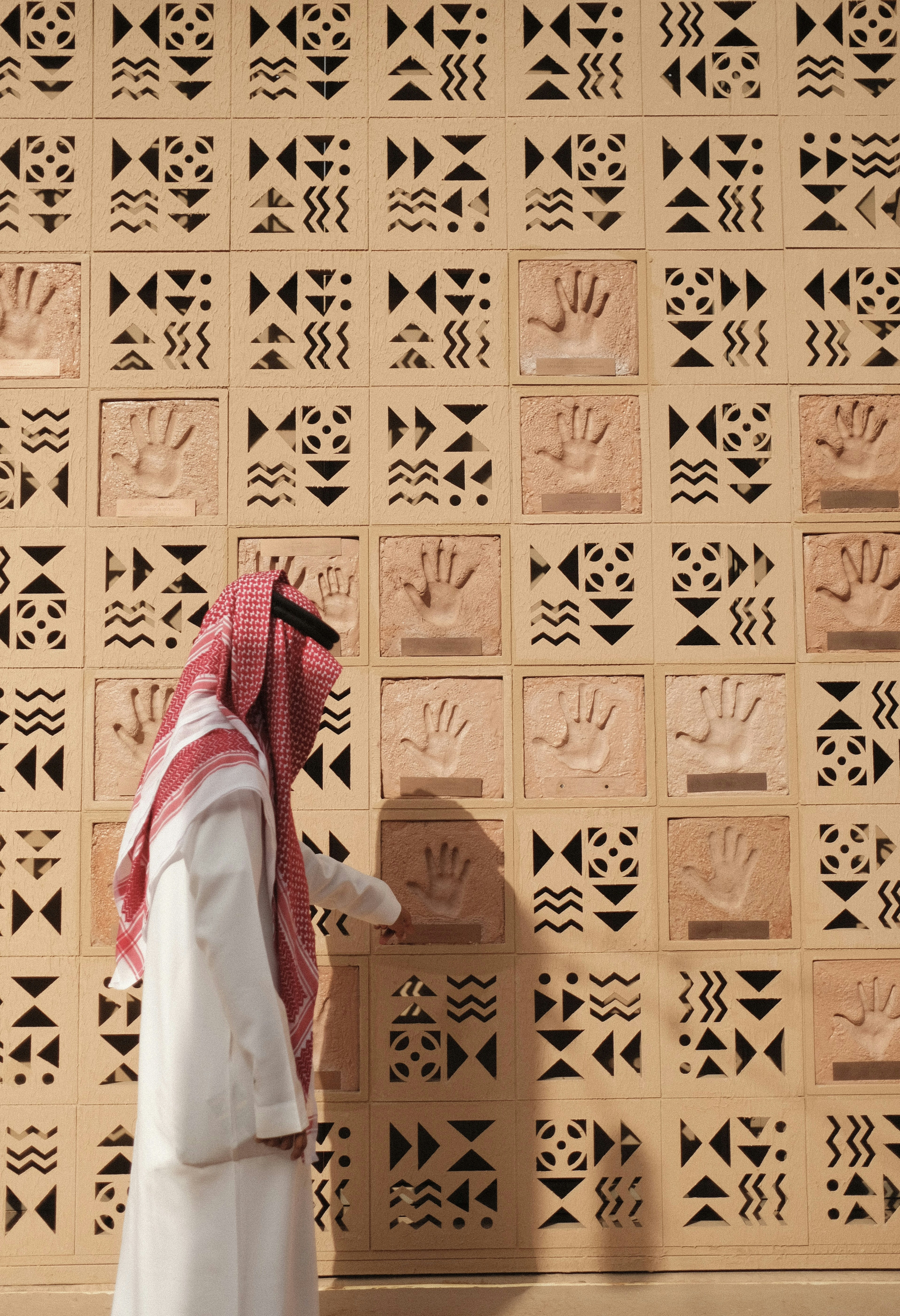 A man examines handprints on a patterned wall.