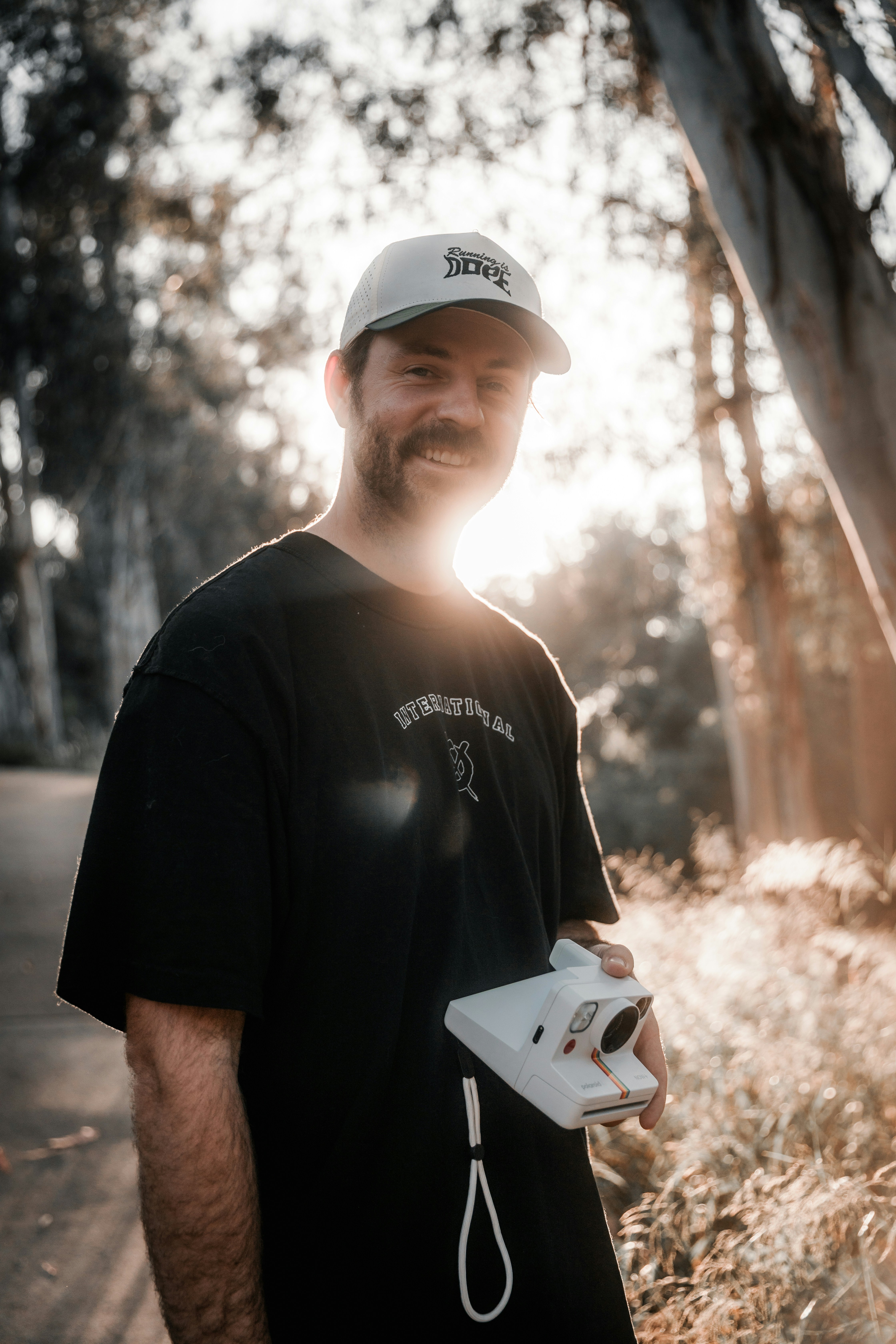 Smiling man holds a polaroid camera outdoors.