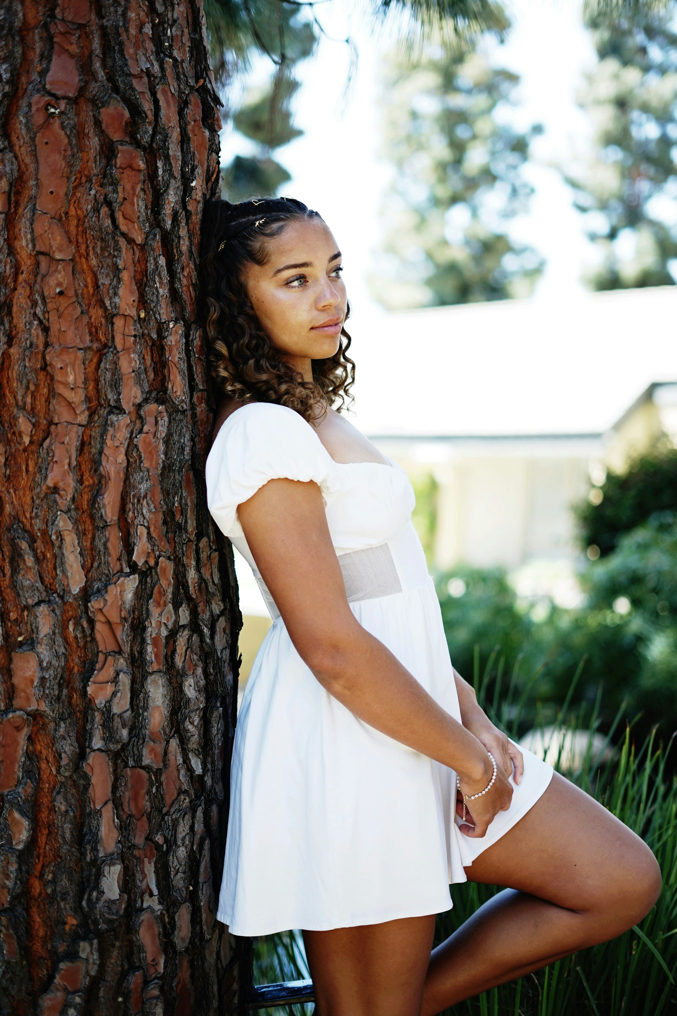 A young woman leans against a tree.