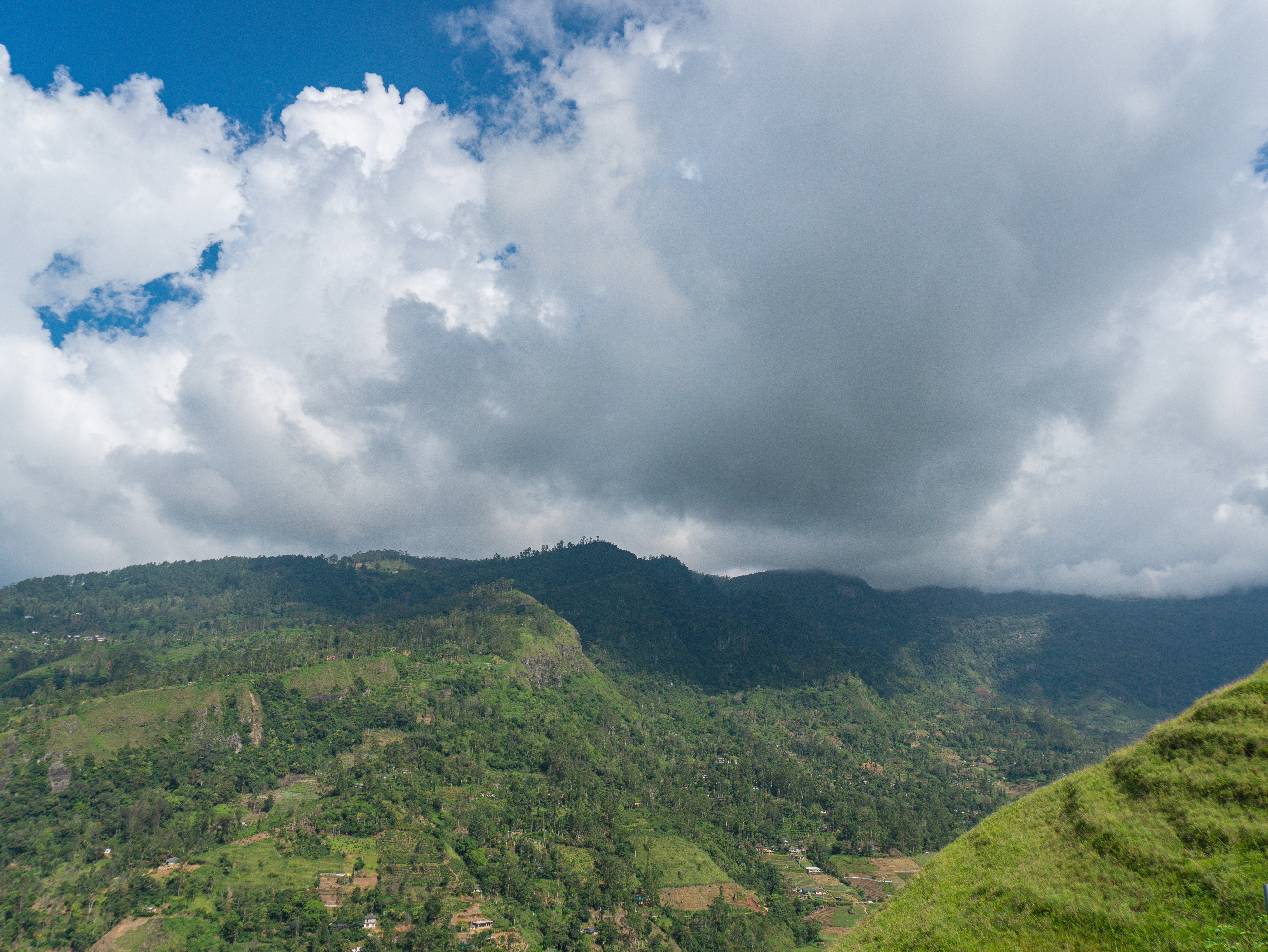 Mountains and green hills are beneath a cloudy sky., Rolling hills covered in emerald tea plantations stretch beneath a dramatic sky dotted with clouds. This Mandaramnuwara panorama captures the timeless beauty of Sri Lanka’s upland landscapes, ideal for lovers of nature and scenic adventure.