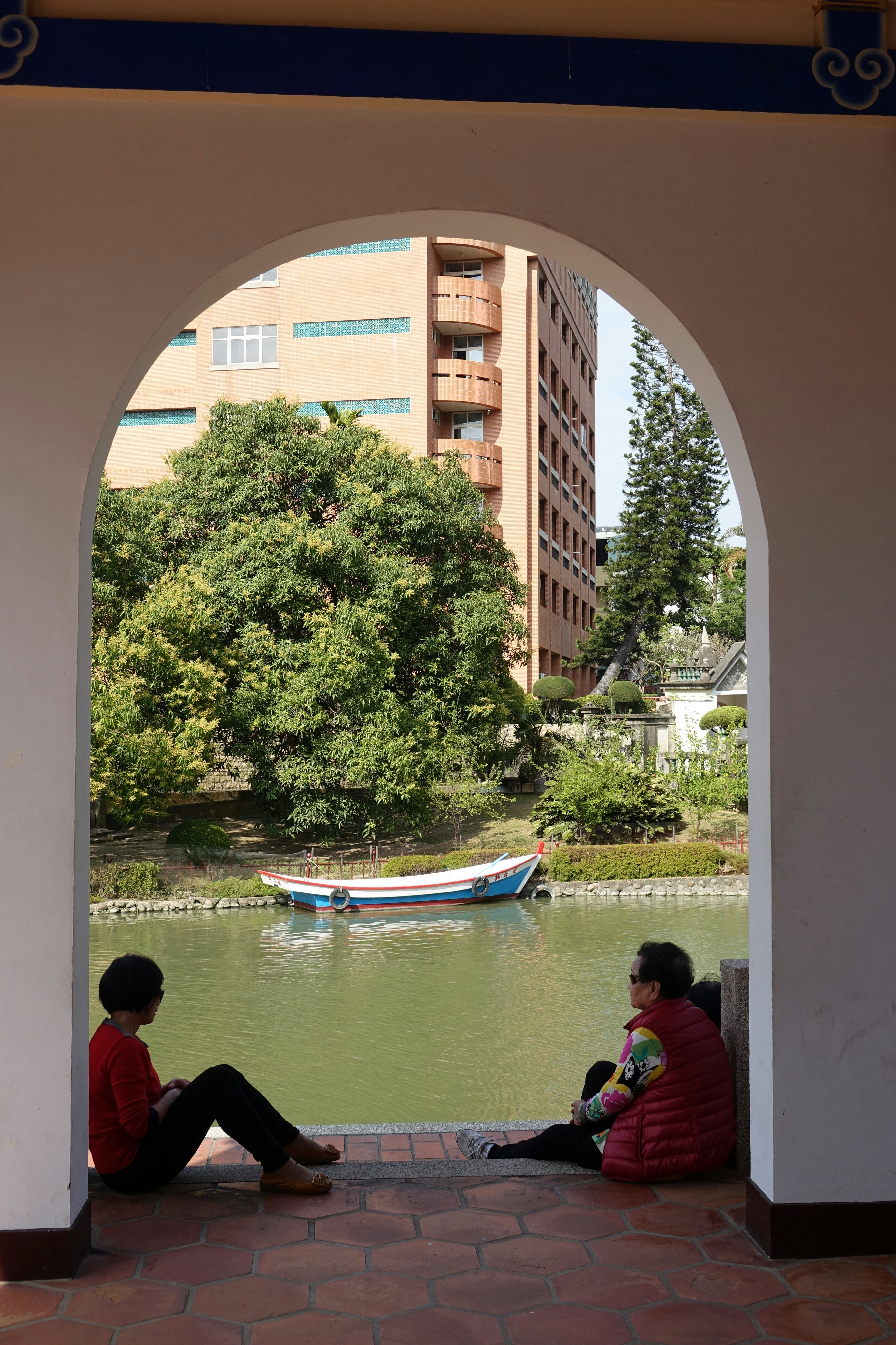 People sit by the water, framed by an arch.