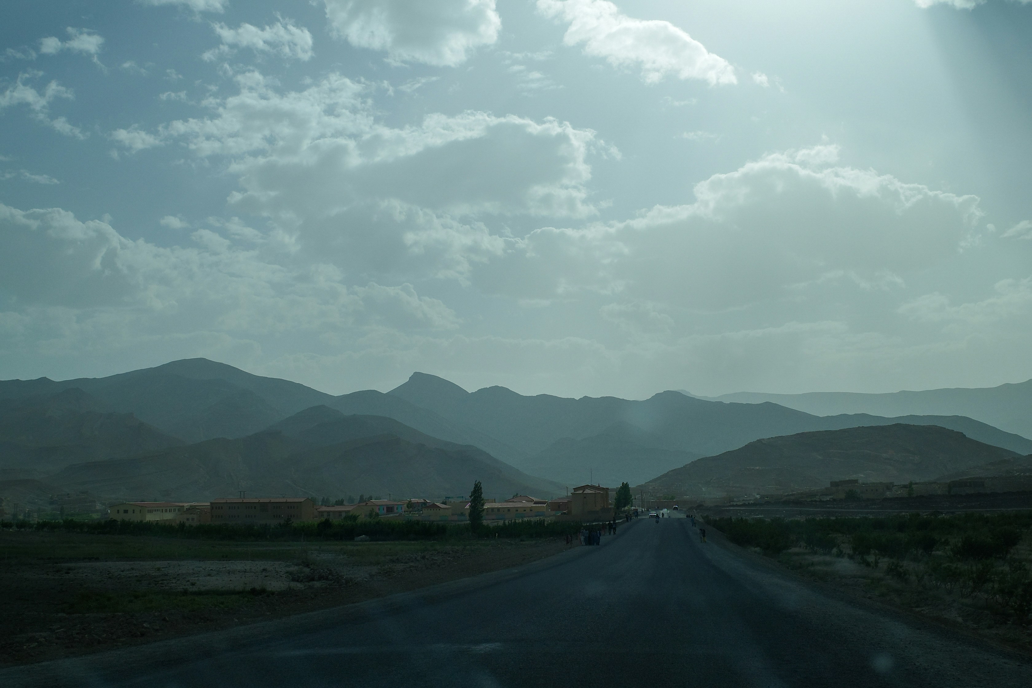 Road leads towards mountains under a cloudy sky.